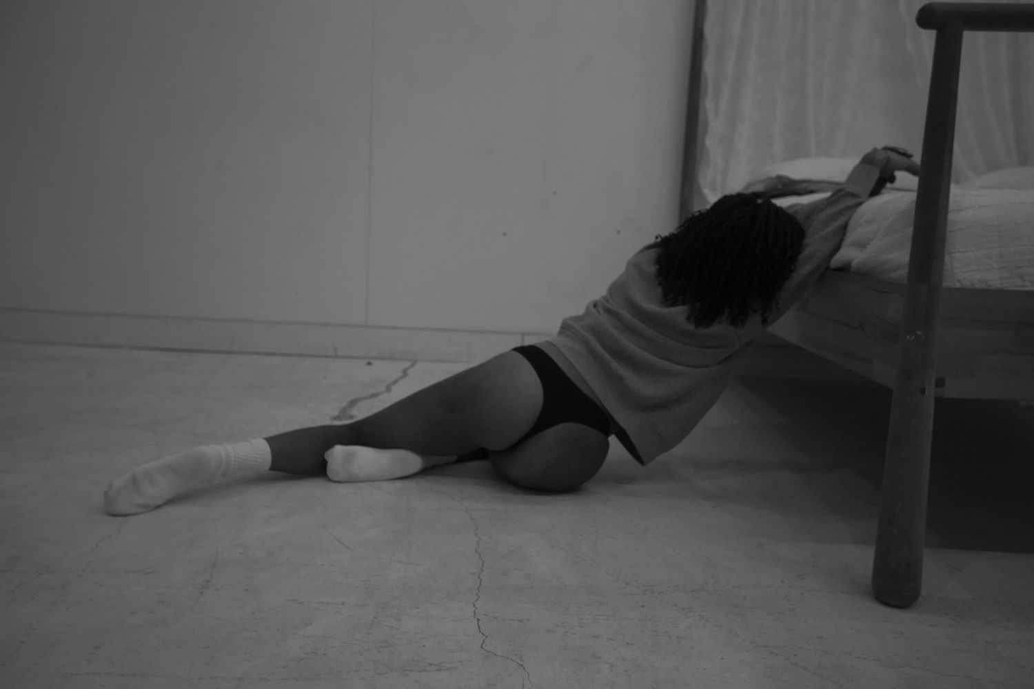 Black and white photo of person lying on floor near wall.