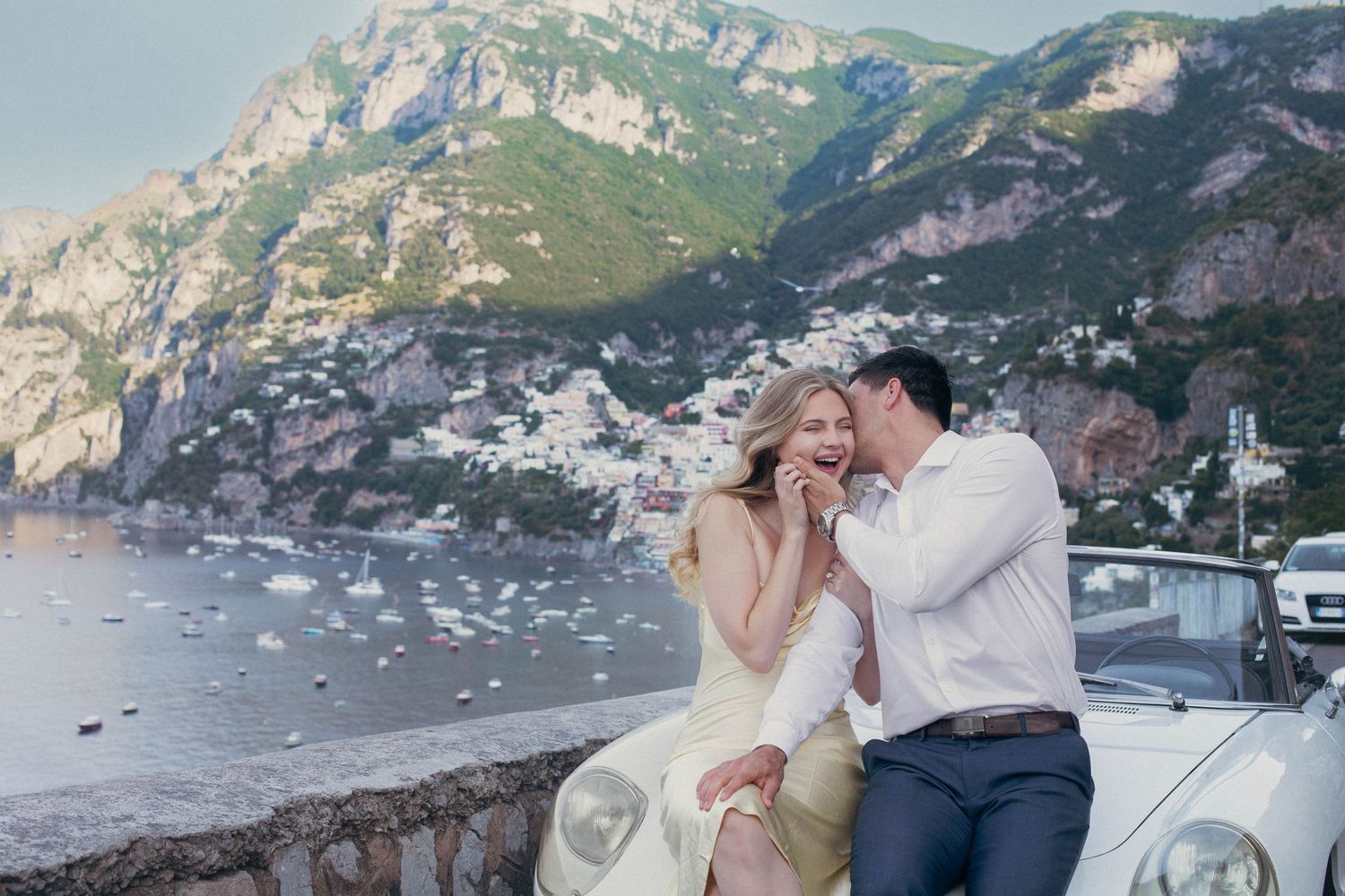 Couple sharing a romantic moment on the Amalfi Coast in Italy, with Positano village and blue sea in the background.