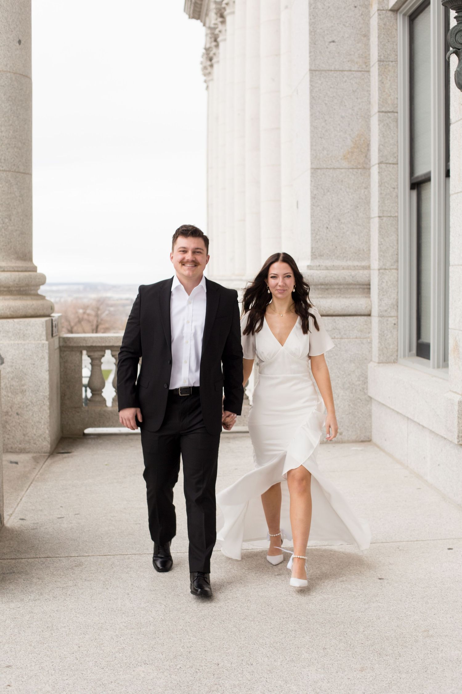 Romantic photoshoot of couple strolling through classical architecture setting.