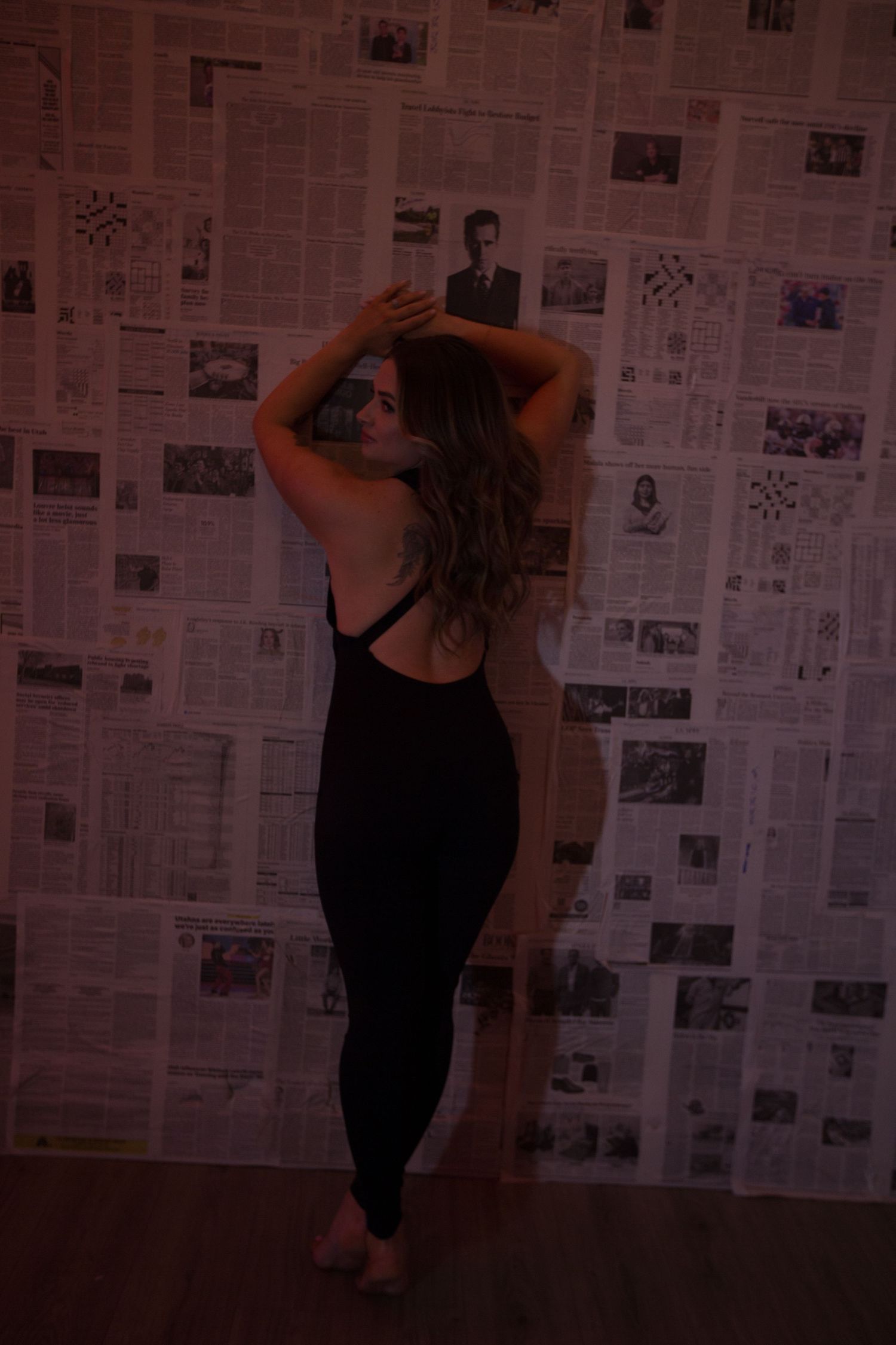 Dancing silhouette photographed against newspaper-covered wall in dim lighting.