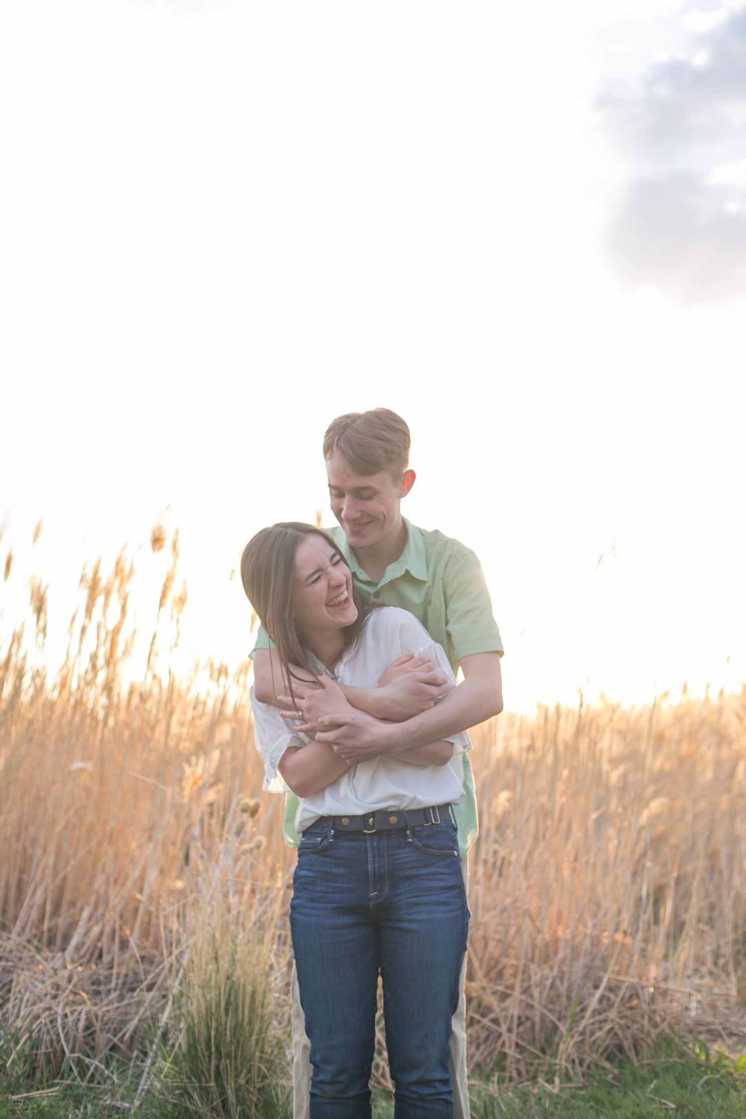 Couple embracing in golden field of tall grass during sunset.