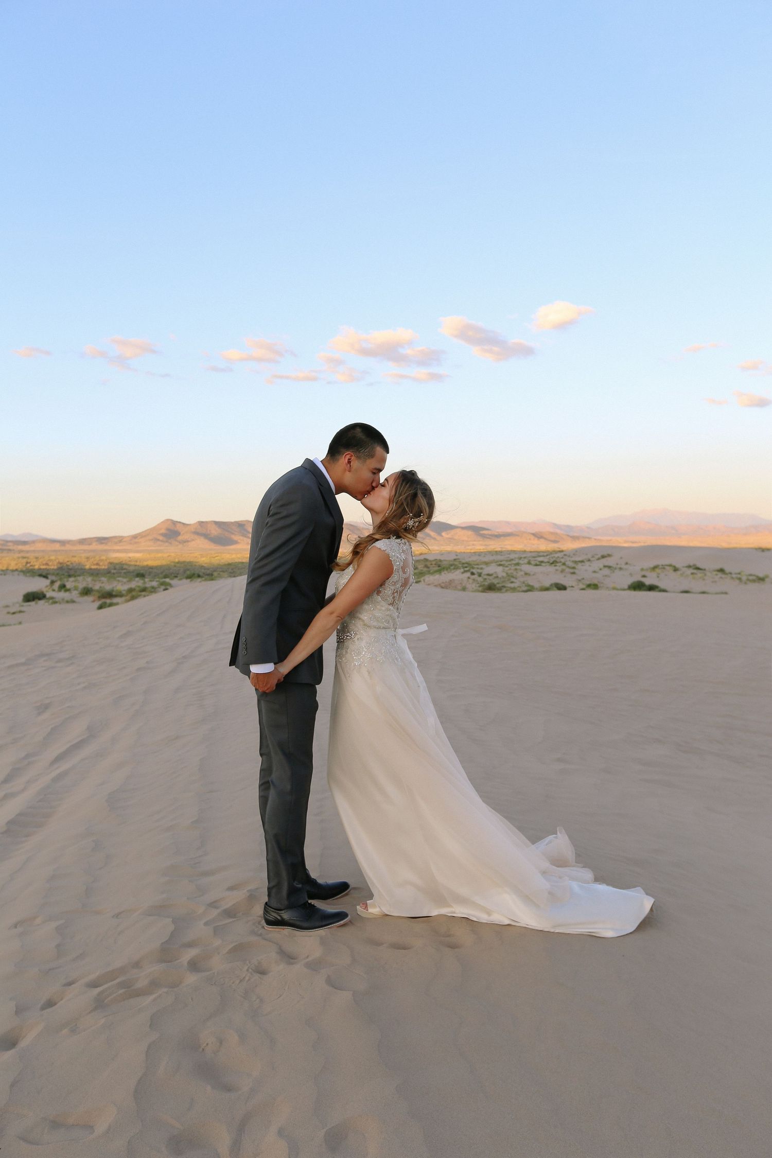 Wedding couple shares intimate moments while posing on sand dunes at dusk.