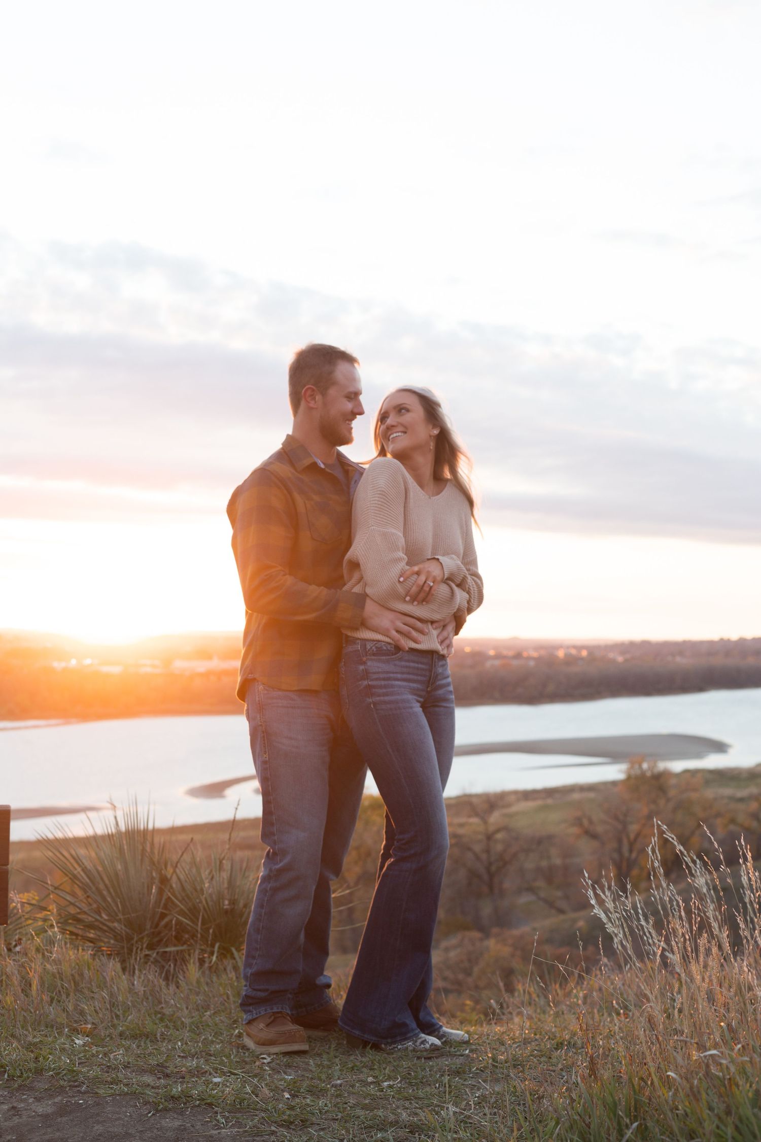 Couple embracing on hilltop during golden hour with coastal view in background.