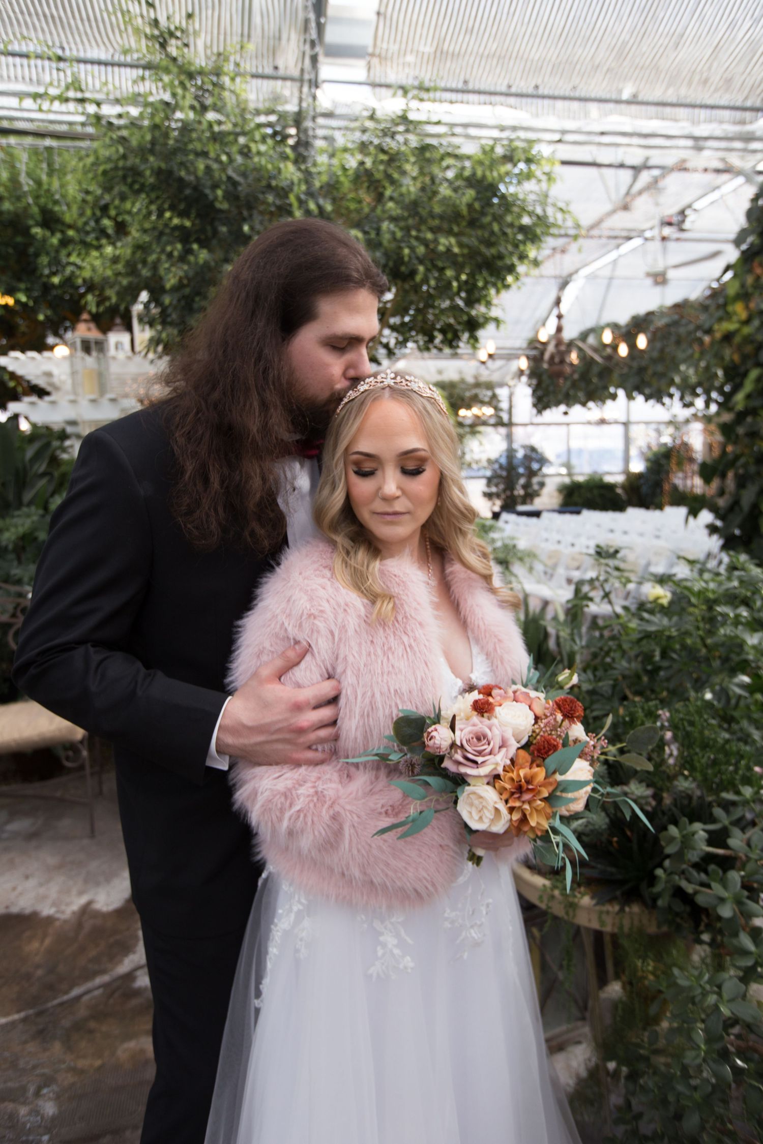 A couple shares an intimate moment in a greenhouse surrounded by plants and roses.