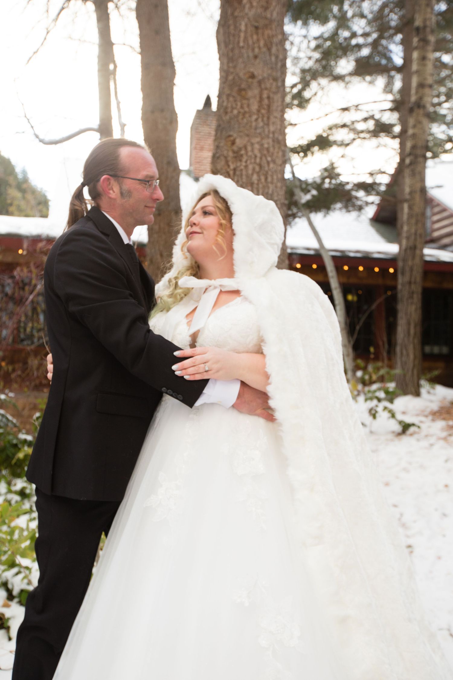 A tender winter wedding moment photographed in front of snow-dusted pine trees.