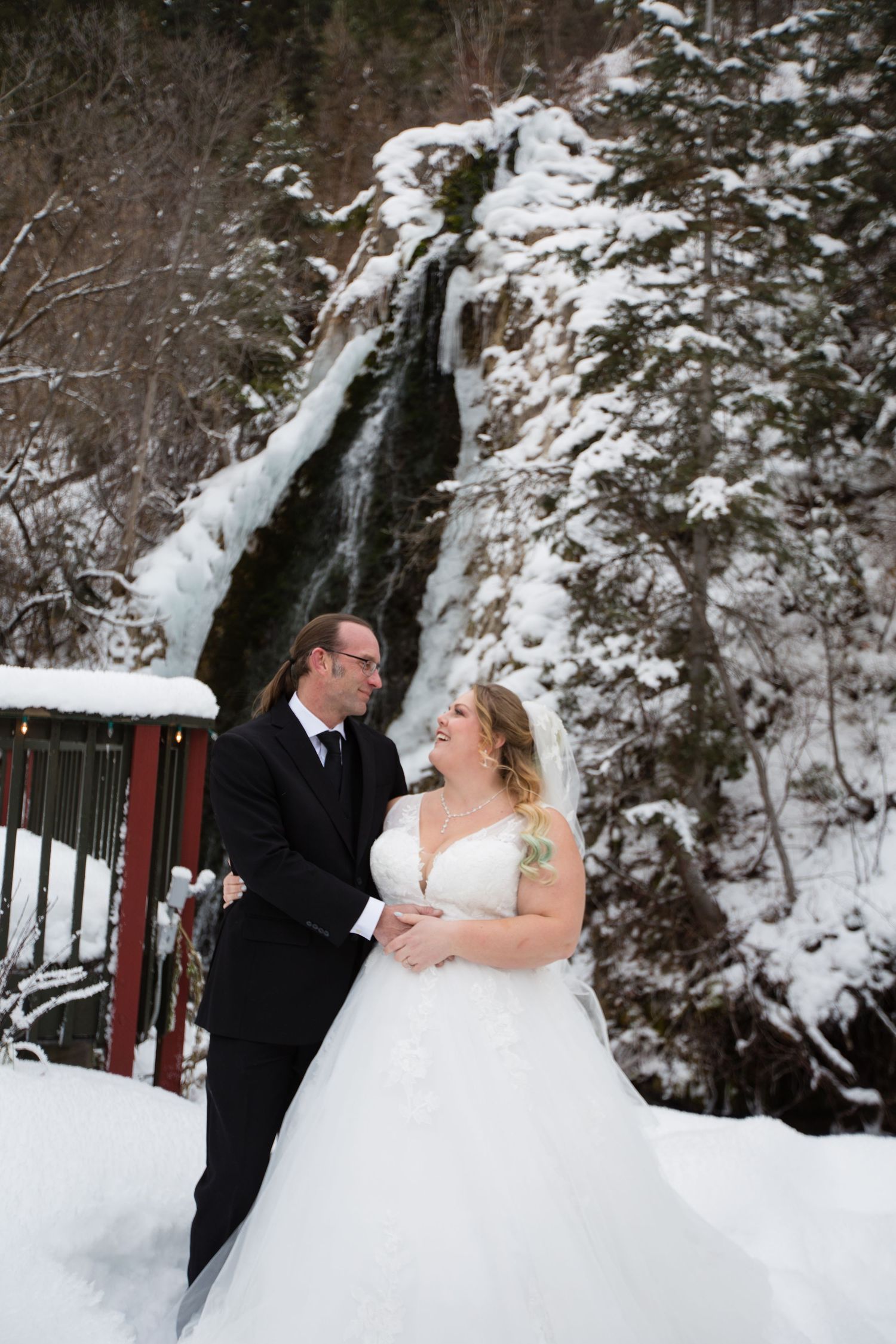 Winter wedding photoshoot in snowy landscape with waterfall backdrop.