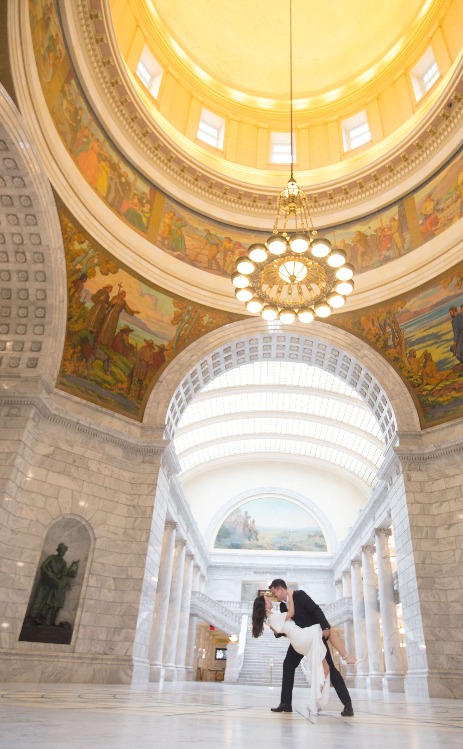 A dramatic dip pose under an ornate domed ceiling with classical murals and chandelier.