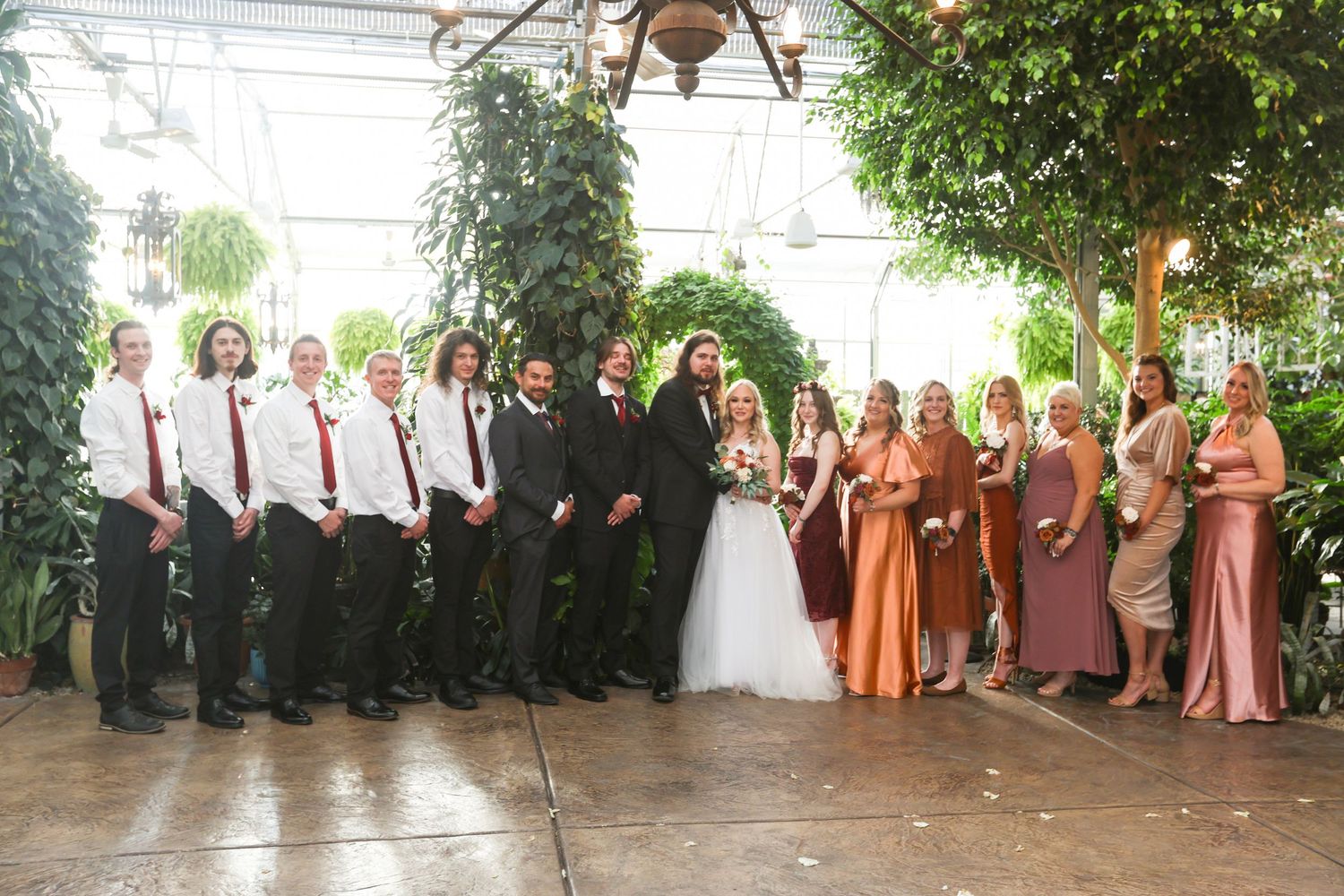 Wedding party poses outdoors in formal attire with bridesmaids in pink dresses and groomsmen in black suits.