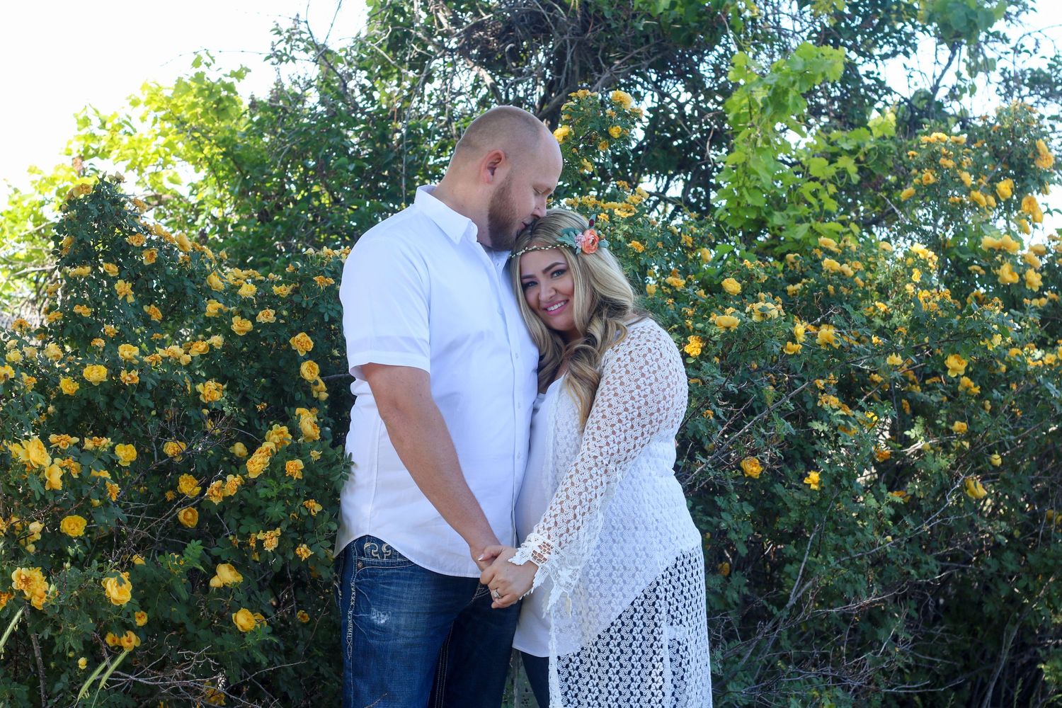 A romantic couple embraces in front of blooming orange citrus trees in a garden setting.
