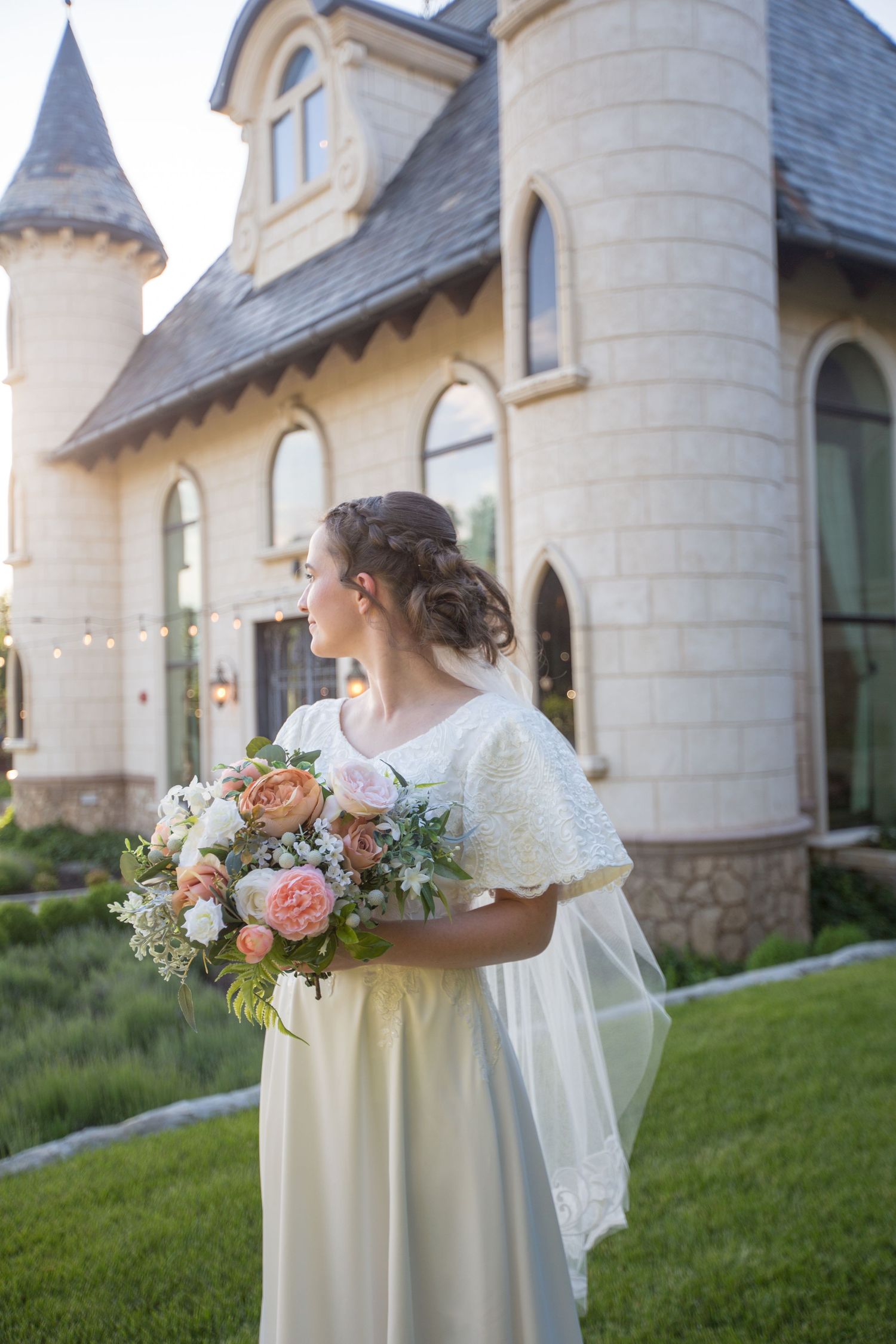 A beautiful bridal bouquet with pink and white flowers rests against a cream colored dress at an elegant venue.