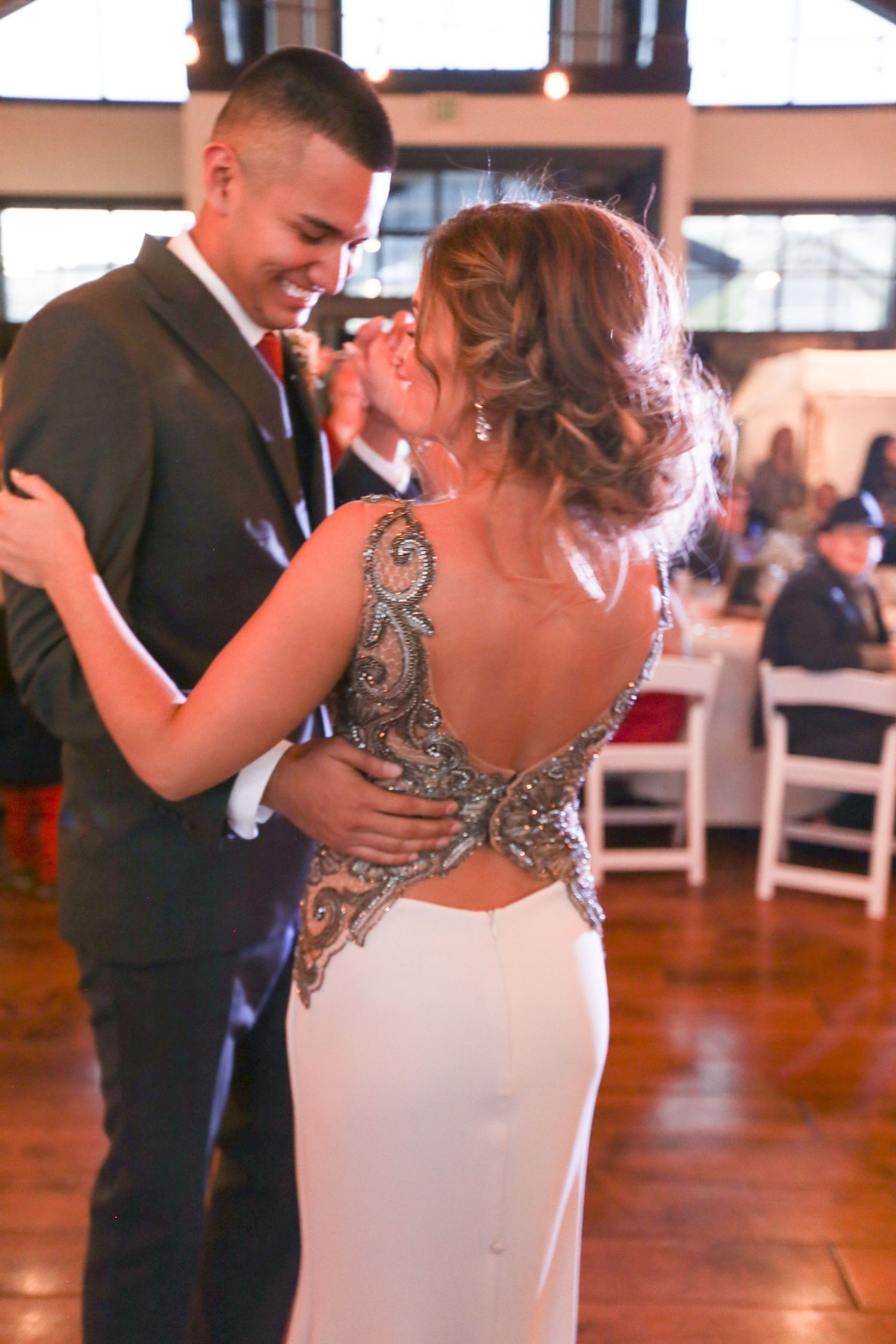 A couple shares their first dance in an elegant reception hall with wooden floors.