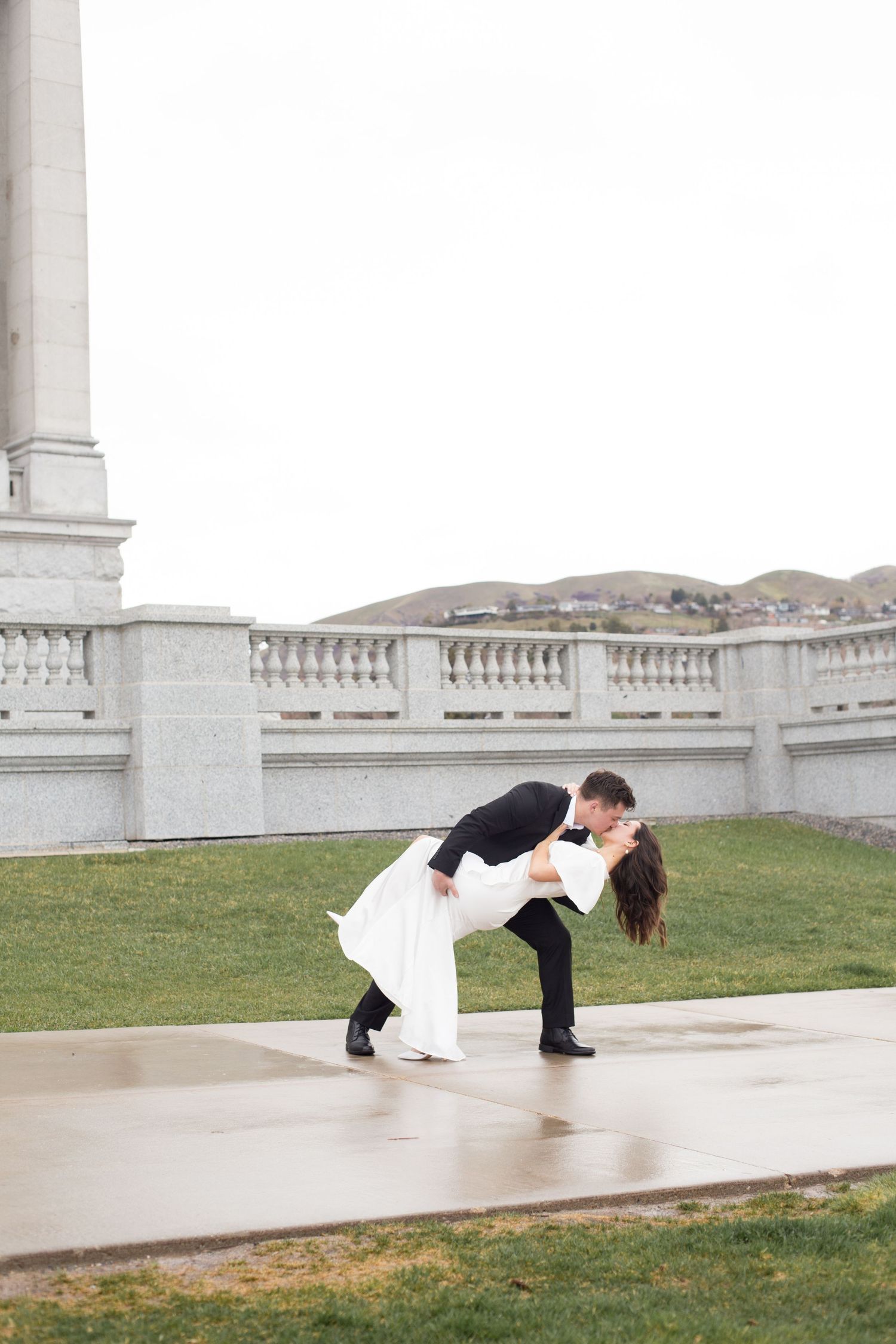 A couple performs a dramatic dip pose on a white stone patio.