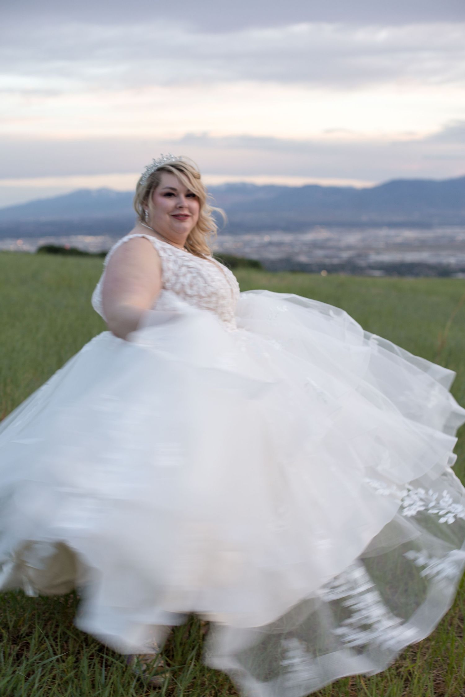 A flowing white wedding dress twirls on a hilltop with mountains in the background.