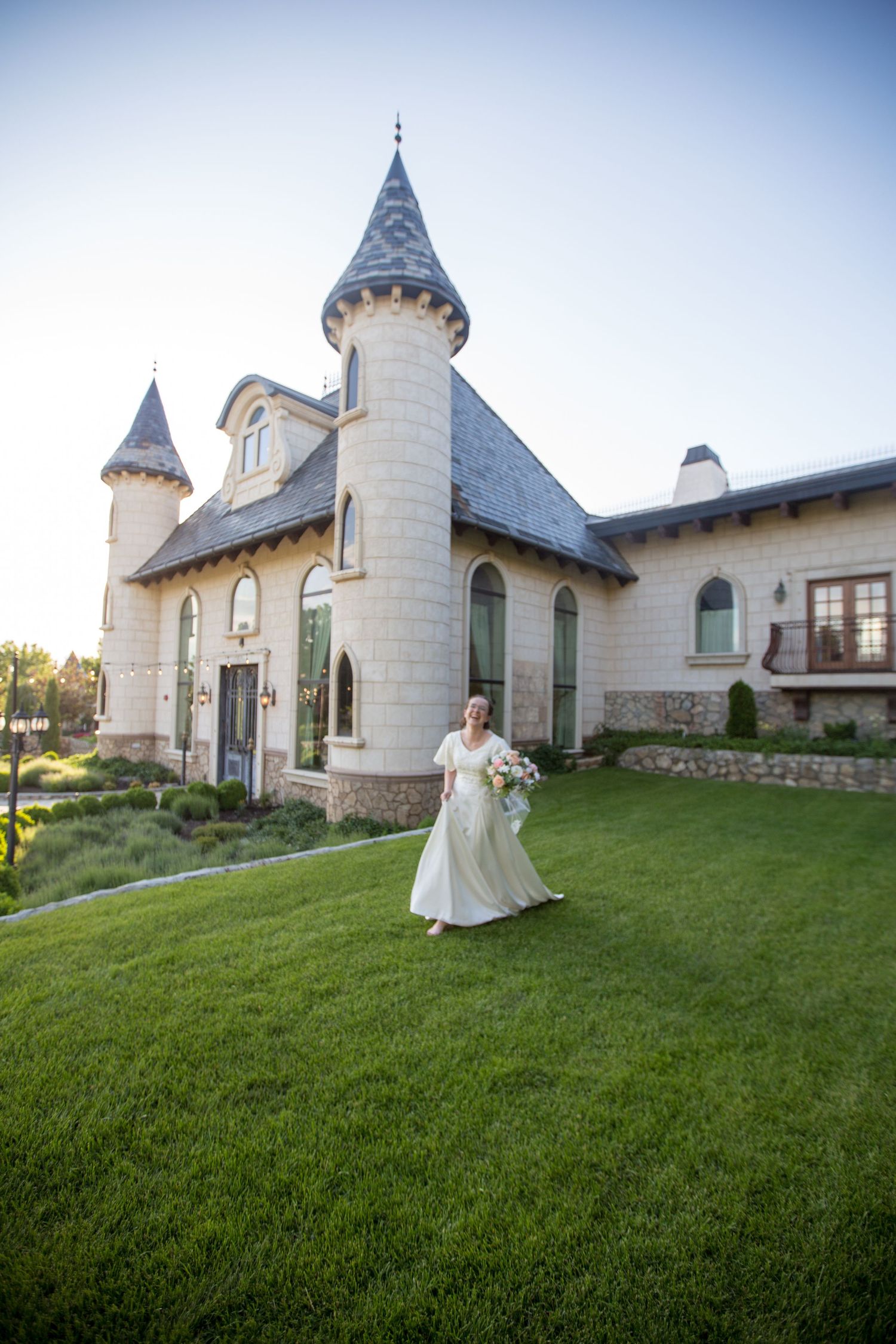 A castle-like wedding venue with stone turrets and a bride in a flowing white dress standing on manicured lawn.