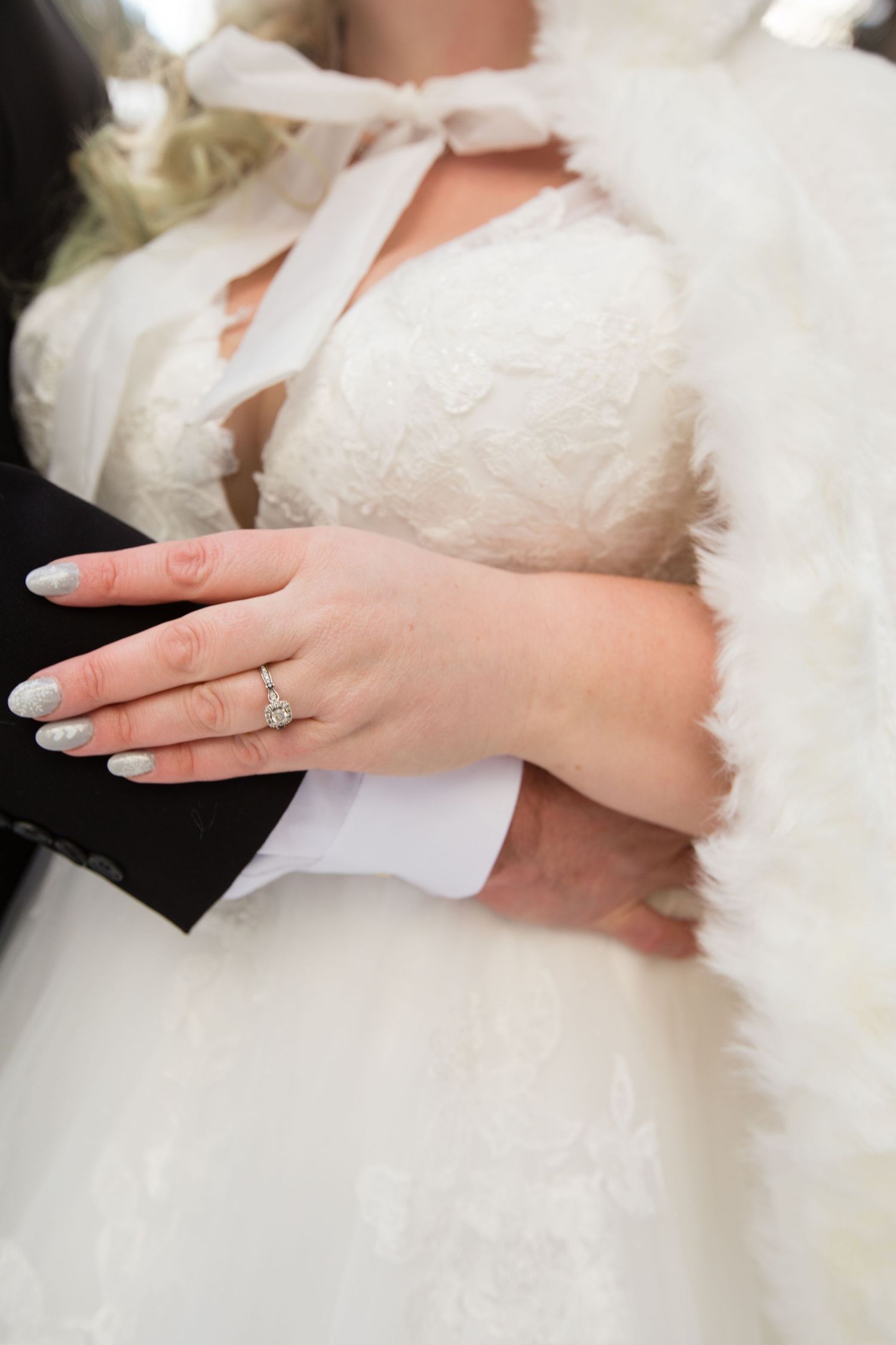 Close-up of a bride's hand showing her engagement ring against her white wedding dress.