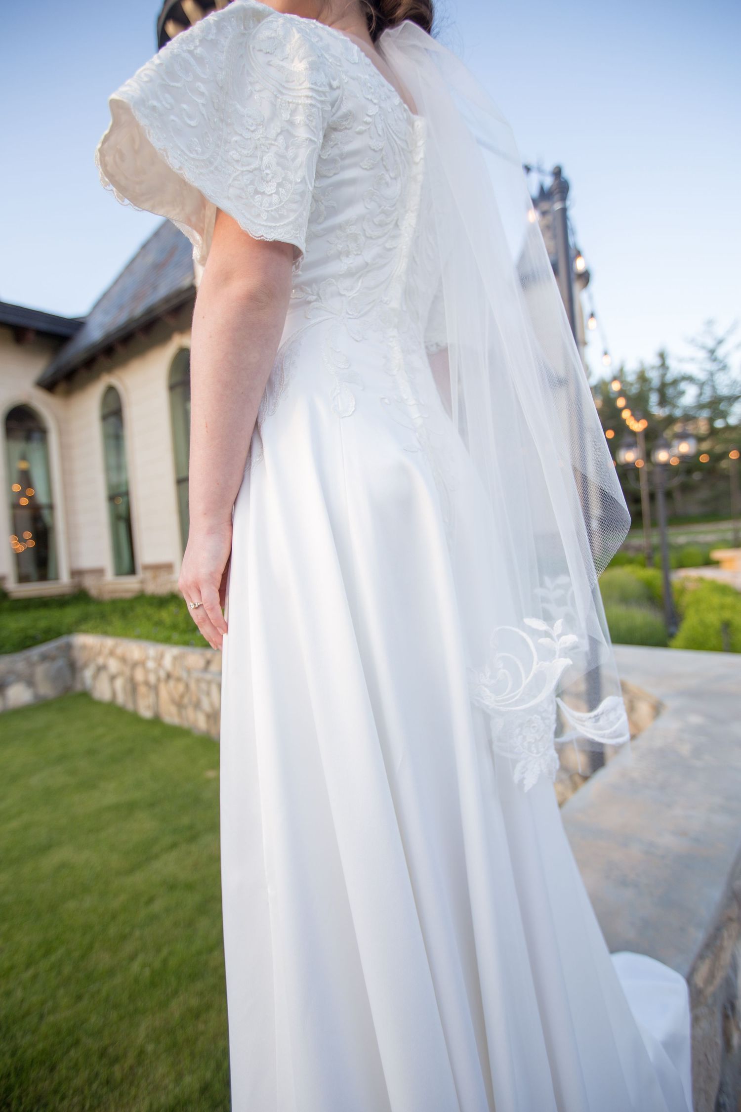 Elegant white wedding dress details against castle grounds.