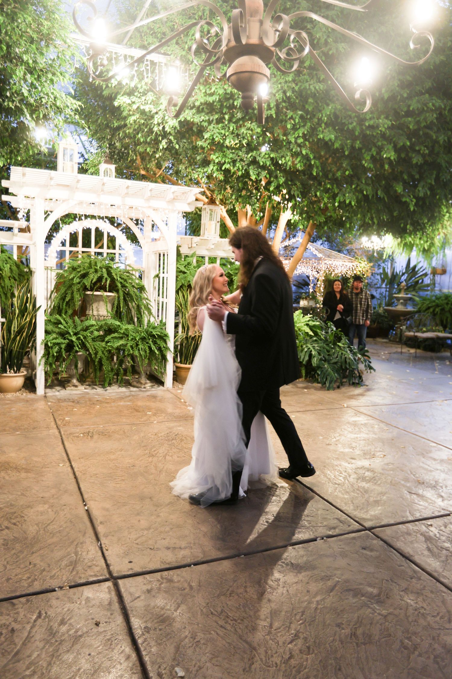 Wedding couple's first dance in greenhouse venue with string lights and natural decor.