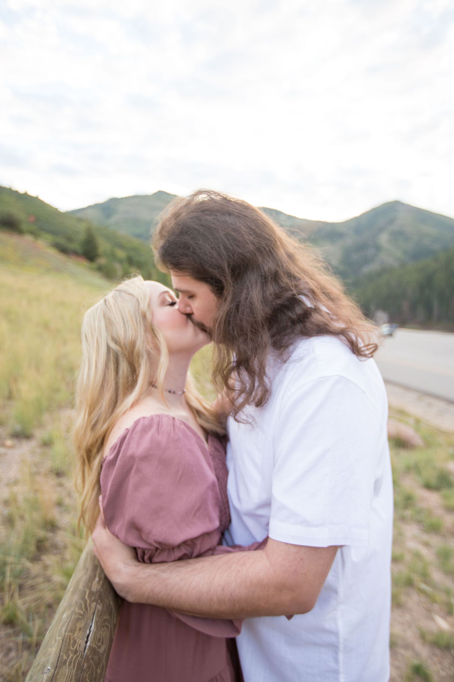 A couple shares an intimate kiss in front of a mountain landscape at golden hour.