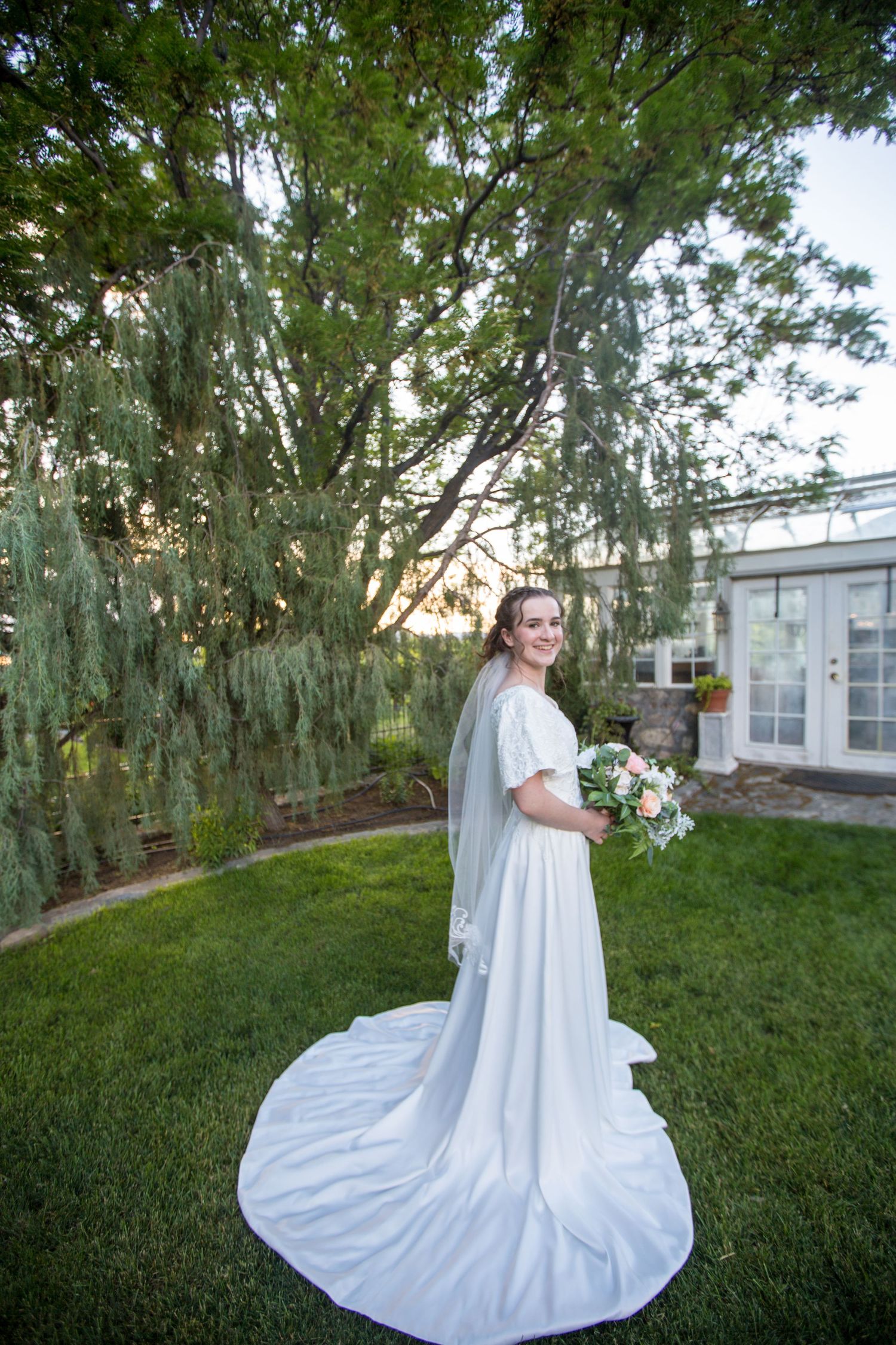 A dramatic white wedding dress with long train photographed in an outdoor garden setting.
