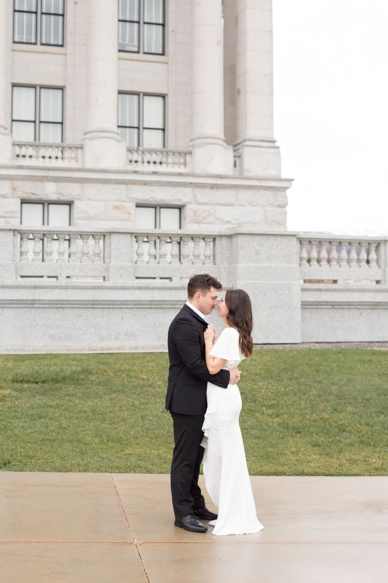 Wedding couple embraces on the grounds of a grand white stone building.