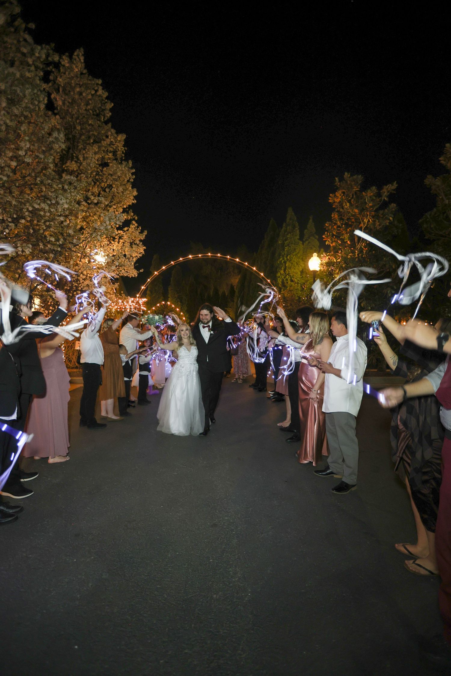 Wedding guests dance with light-up wands in a dark outdoor reception area.