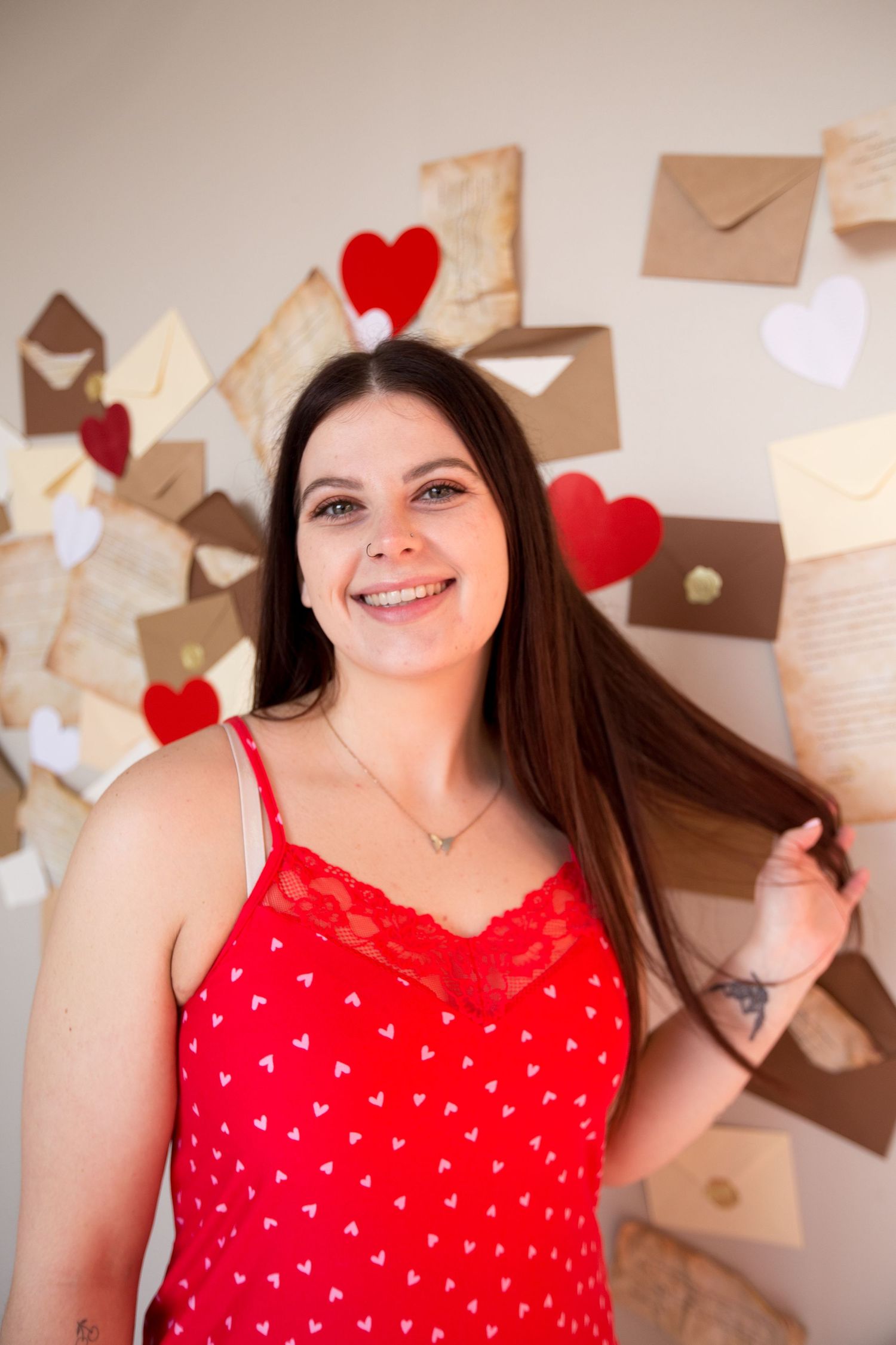 Woman in red heart-print dress smiling against wall of vintage letters and hearts.