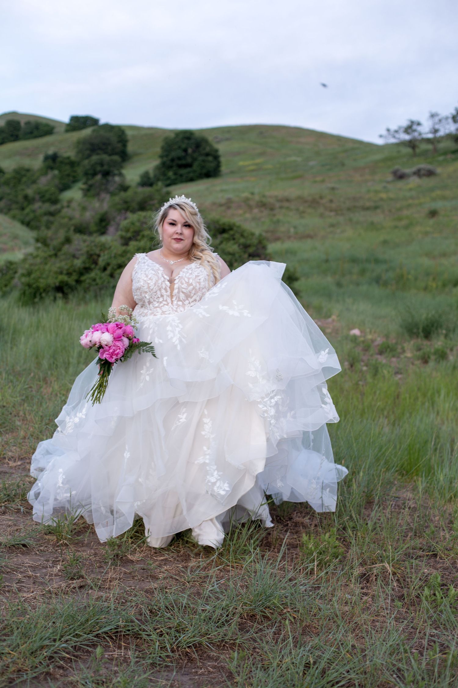 A wedding dress with layers of tulle and lace against a green hillside landscape.