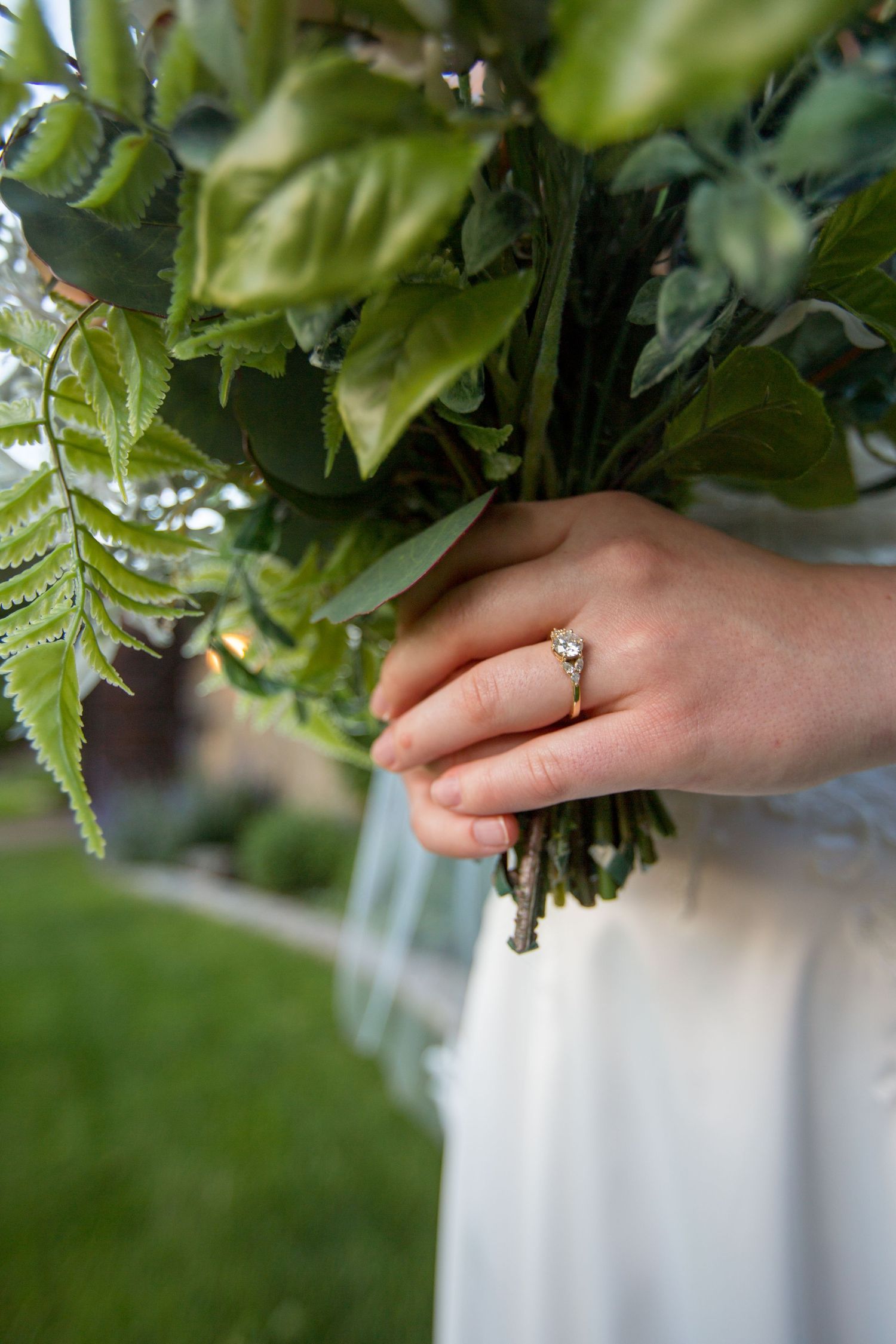Close-up of hands holding a delicate floral bouquet with greenery against a light background.