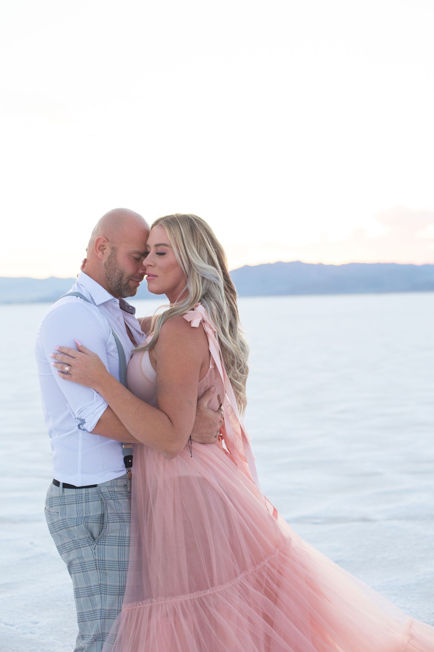 Couple shares intimate embrace against serene ocean backdrop.
