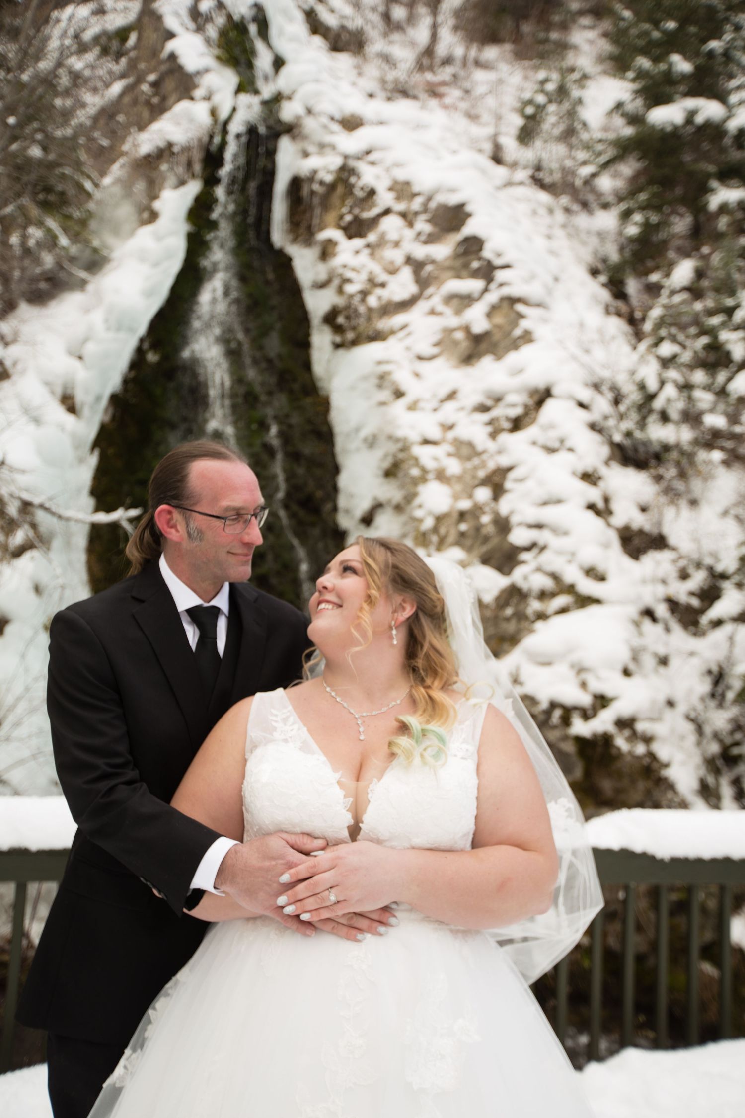 Winter wedding portrait on a wooden deck with snow-covered cliffs in the background.