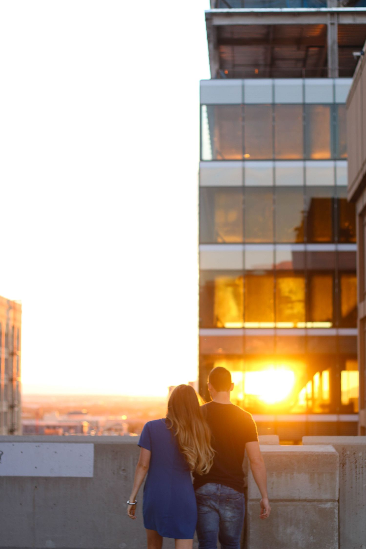 A couple watches the sunset together against a modern building backdrop.