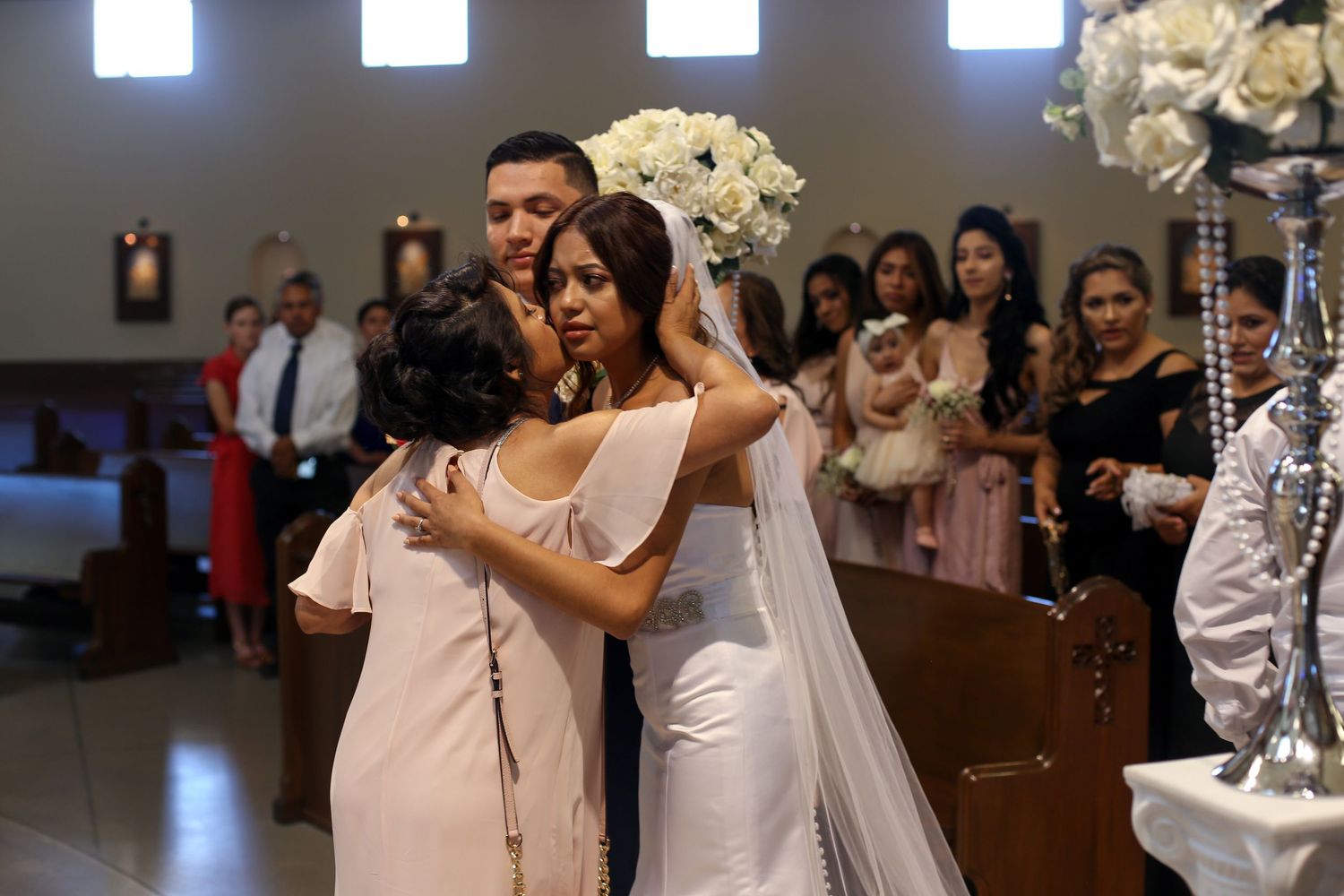 An emotional embrace during a wedding ceremony in a church decorated with white floral arrangements.