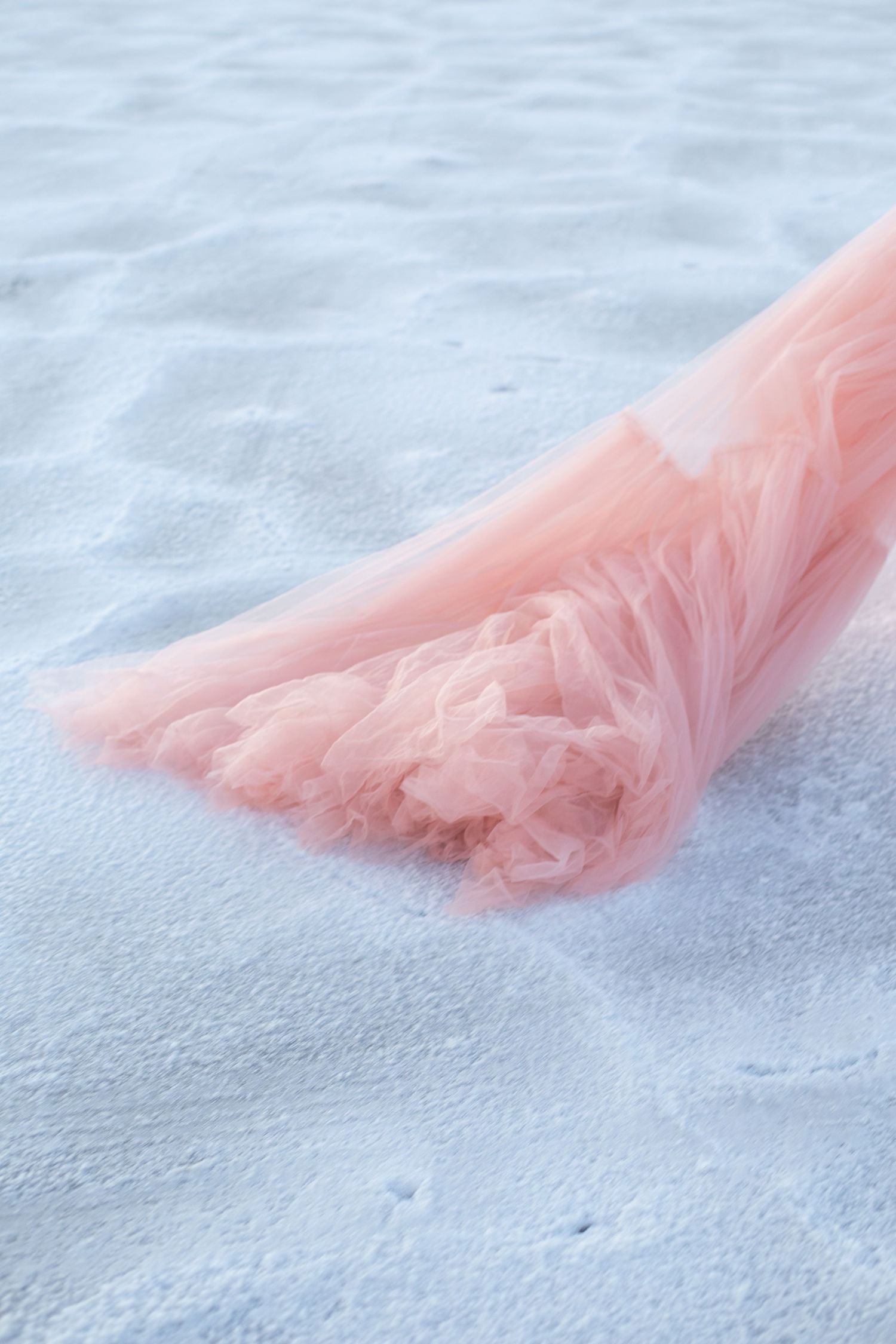 Pink tulle dress fabric flows across white sandy beach.