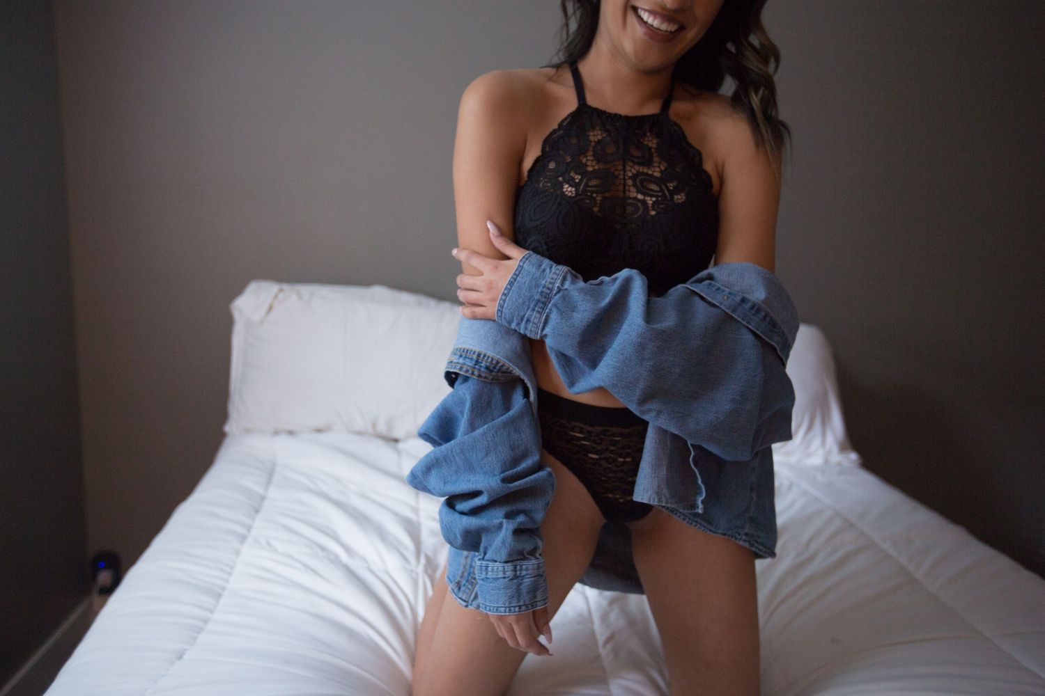 Person in black top holding blue denim jeans while sitting on white bed.