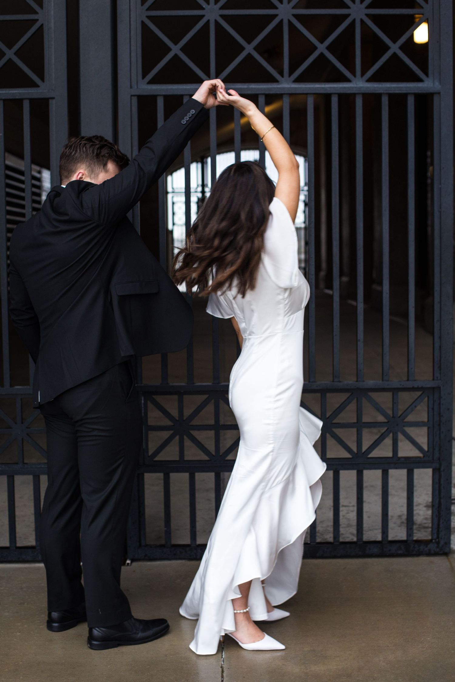 Dancing couple in black and white formal wear pose dramatically by metal gates.
