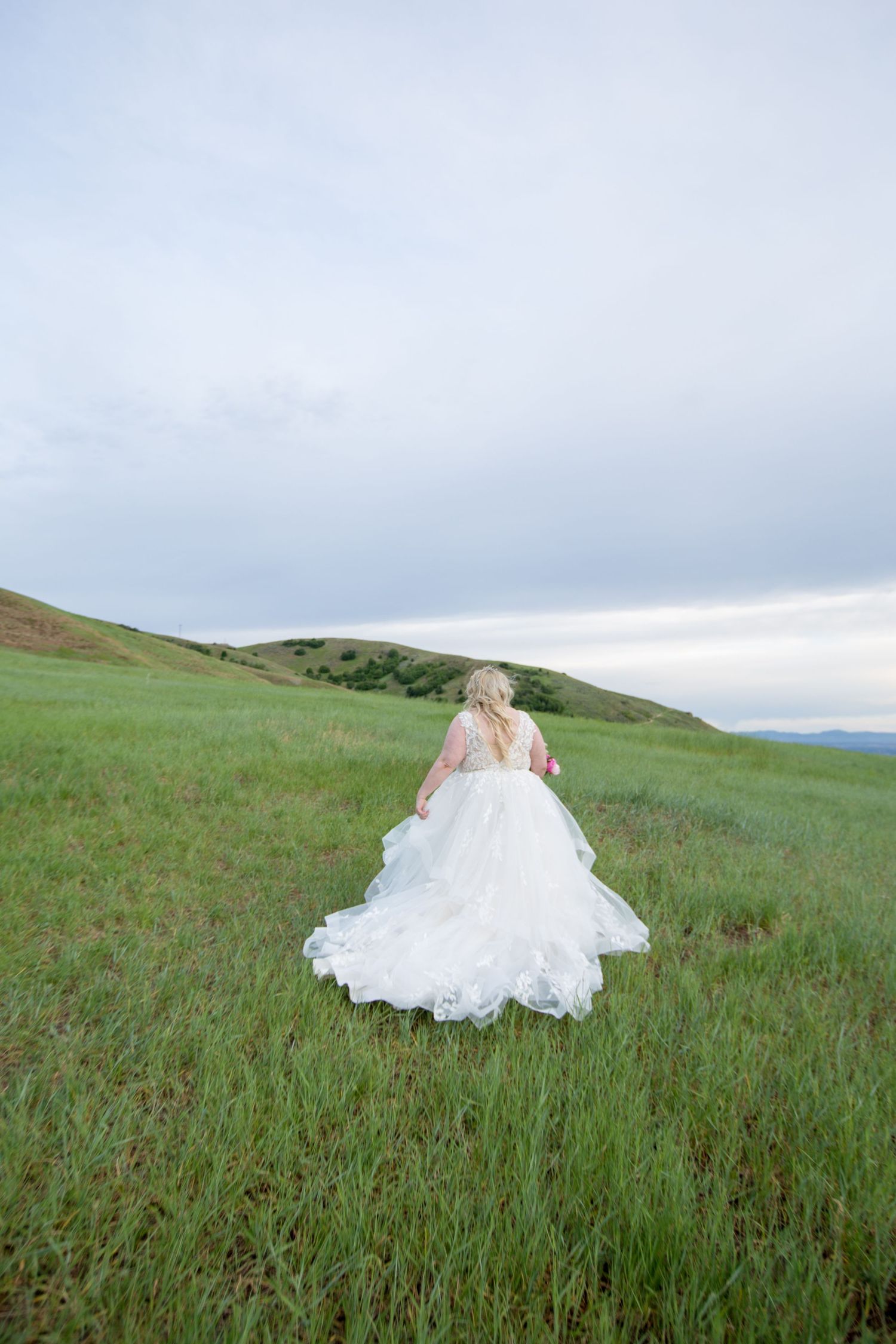 White wedding gown creates dramatic silhouette against rolling green countryside.