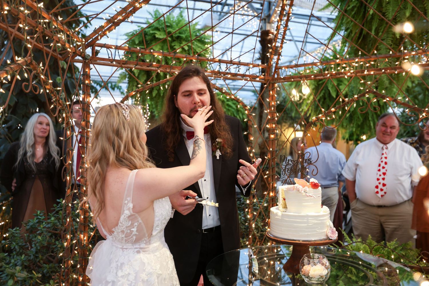 Wedding celebration in a greenhouse decorated with twinkle lights and natural greenery.