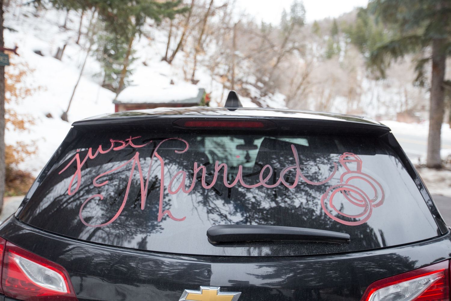 Just Married written on rear car window of Chevrolet SUV in snowy mountain setting.