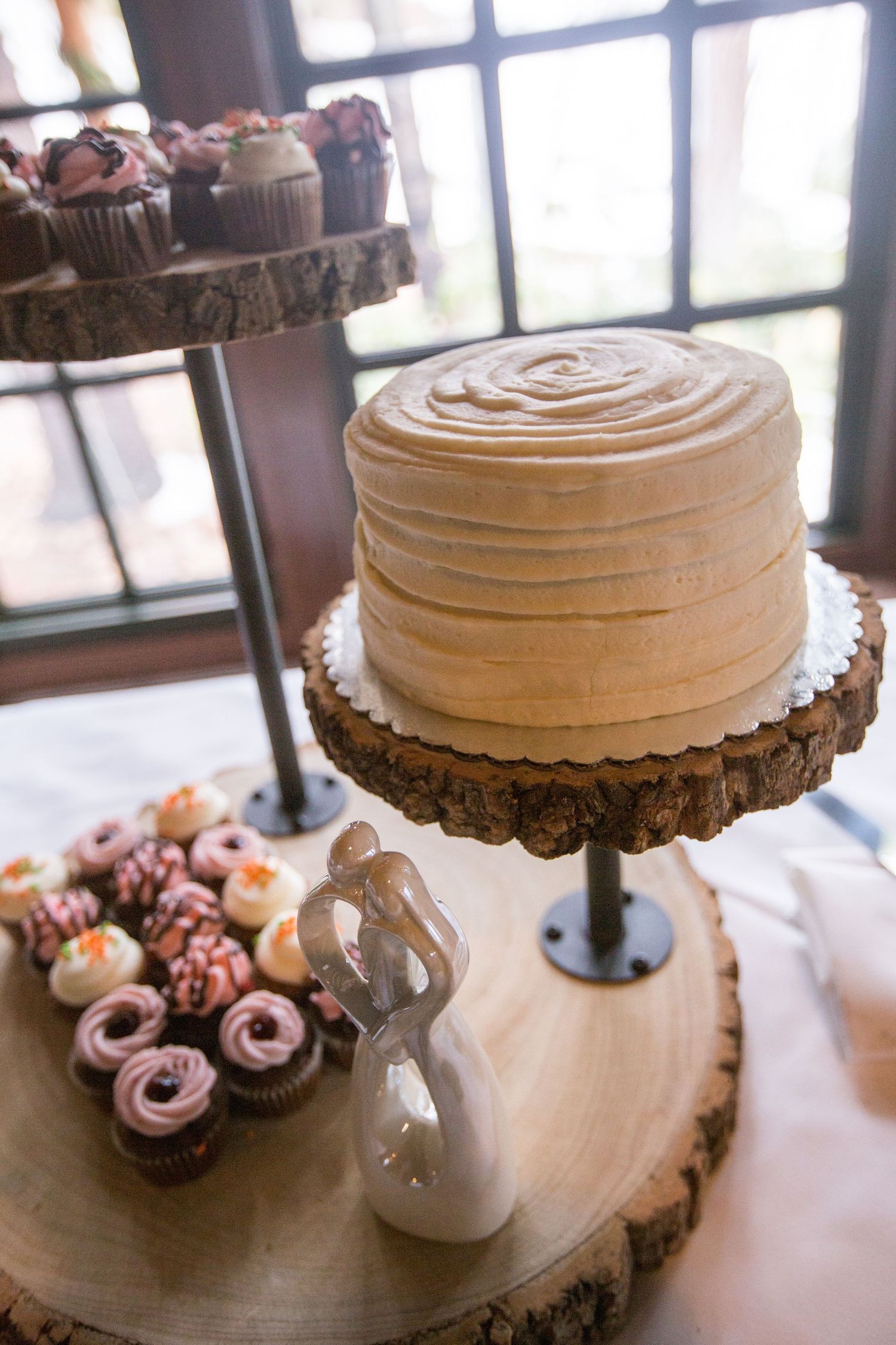 Rustic wedding dessert table with caramel frosted cake on wood stand, cupcake tower, and bride and groom topper.