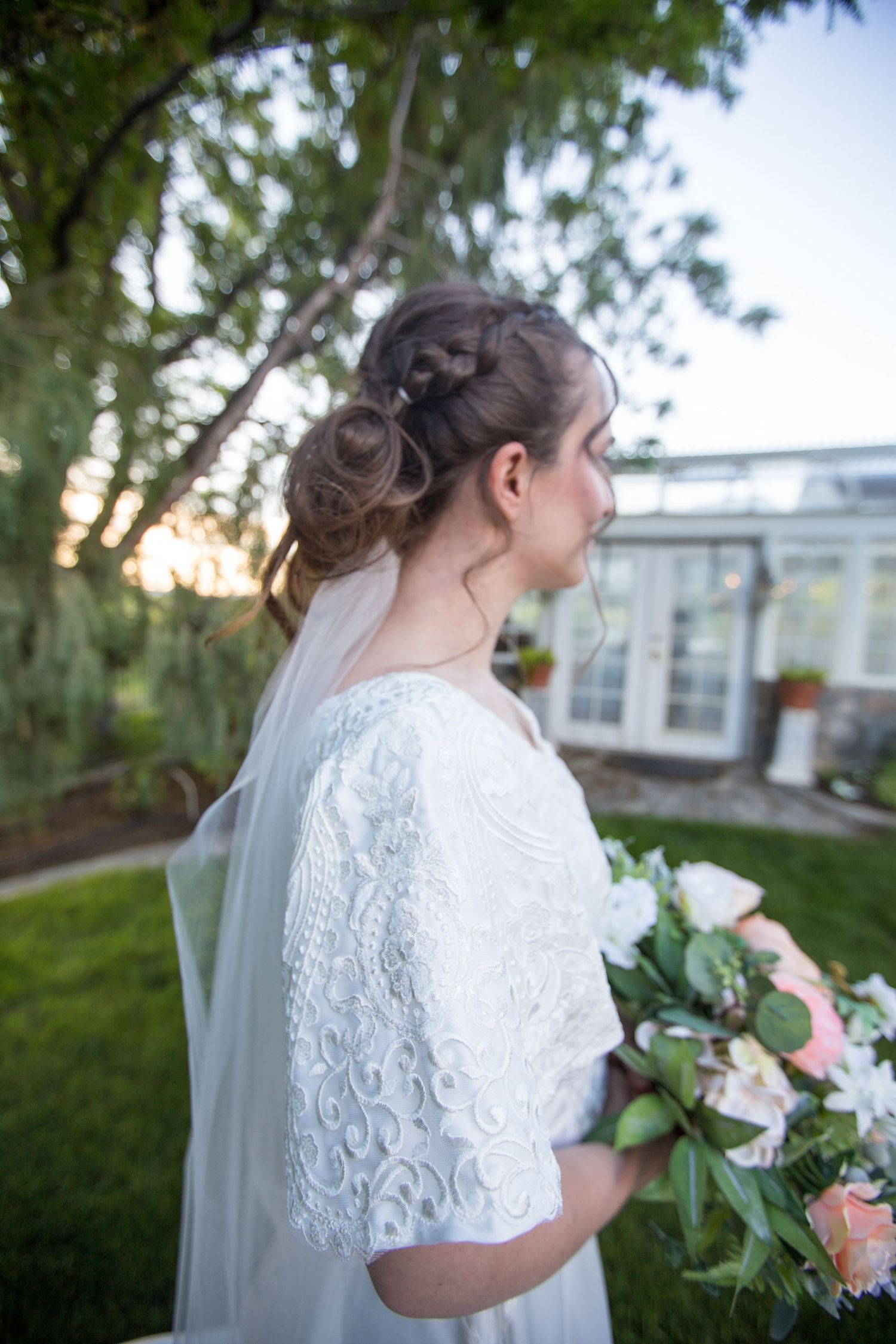 Delicate lace details of a white wedding dress with pink and white floral bouquet.
