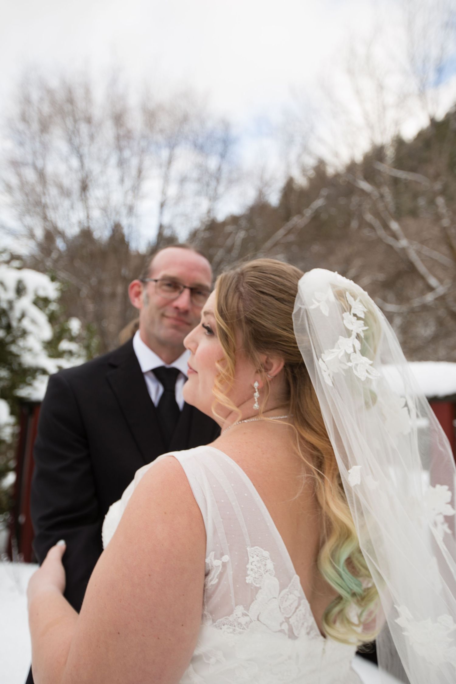 Wedding couple embraces during their winter ceremony with snow covered trees in background.