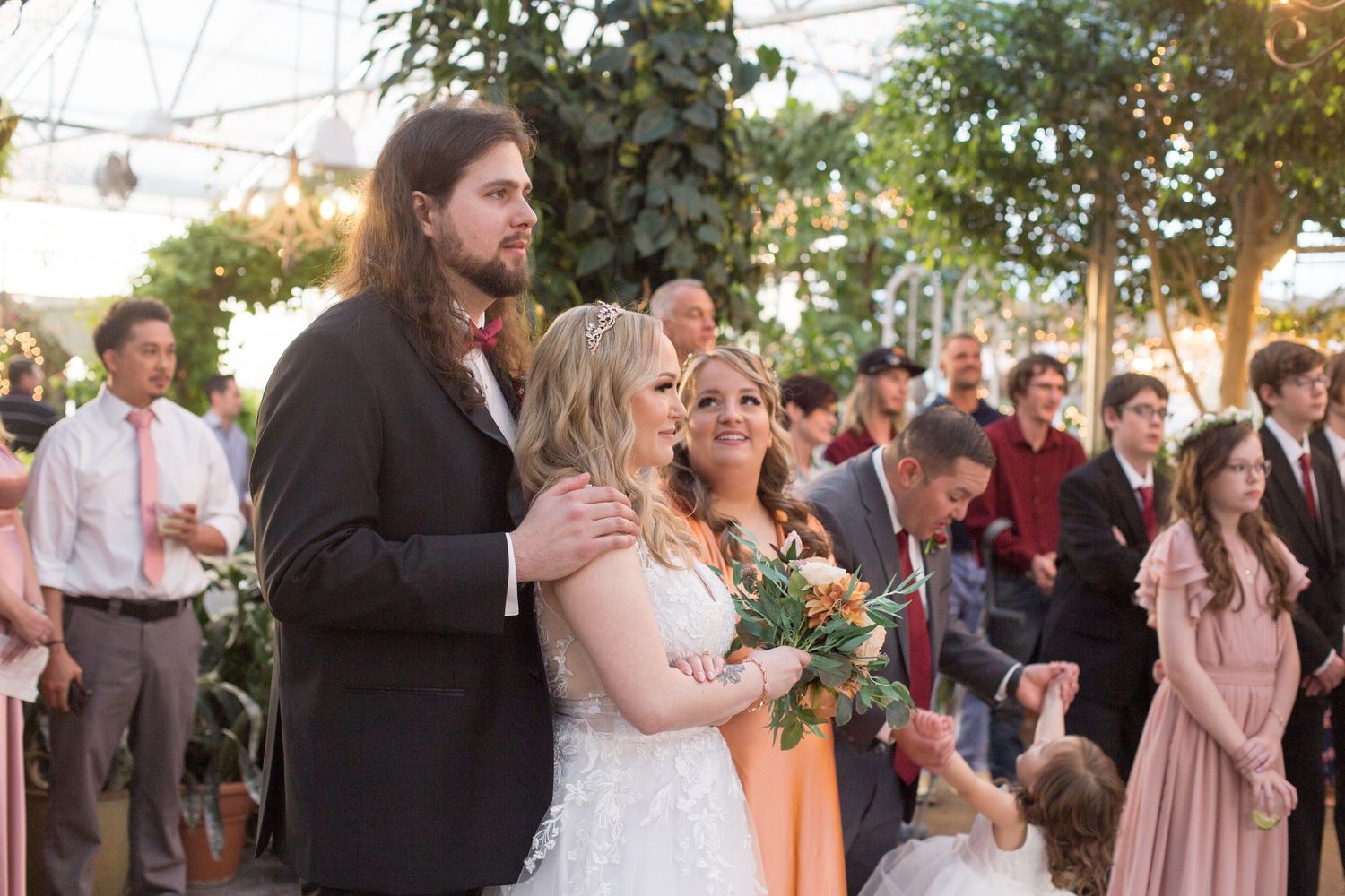 Wedding reception celebration with guests gathered outdoors under string lights.