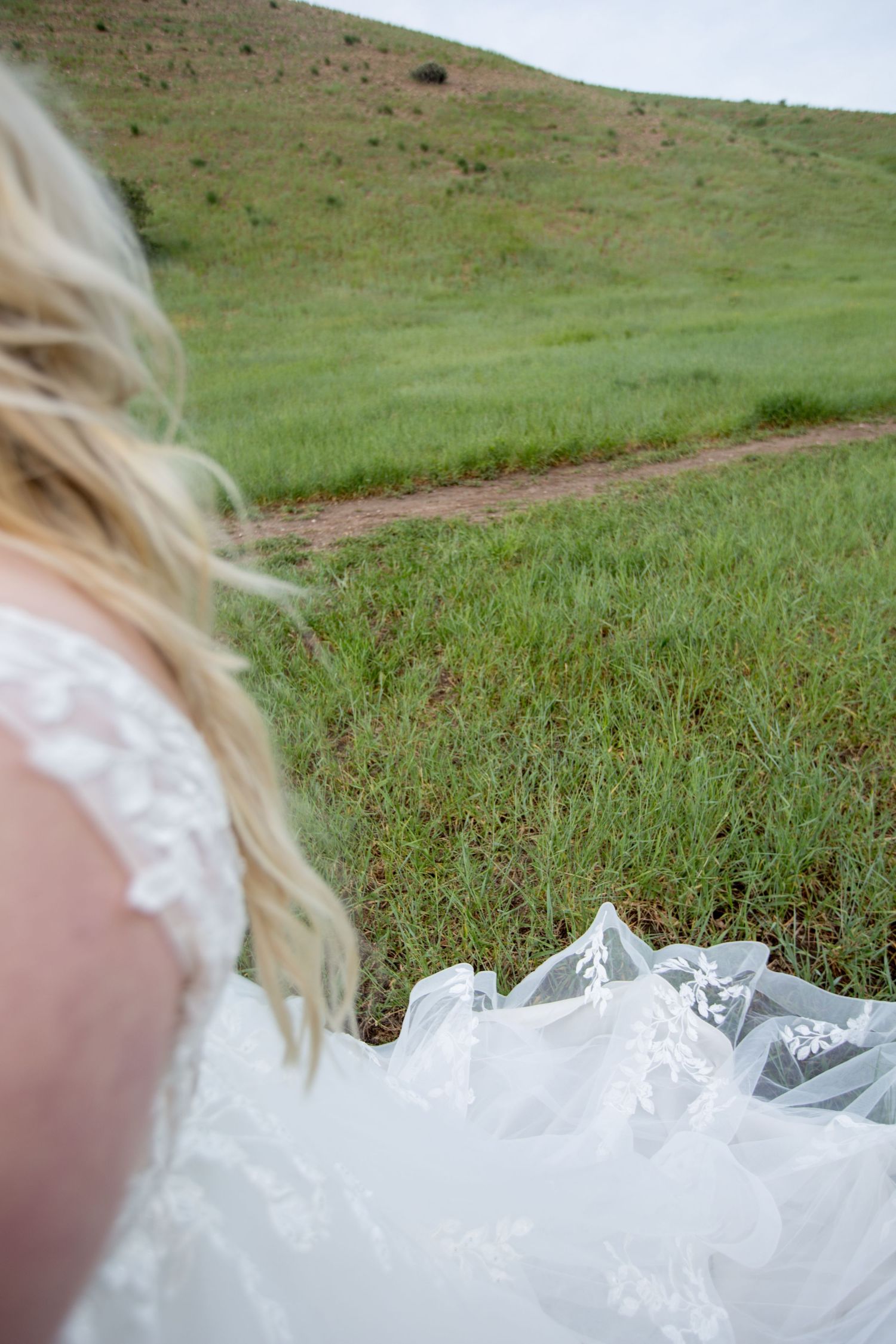 Artistic detail shot of flowing white wedding dress fabric against green grass.