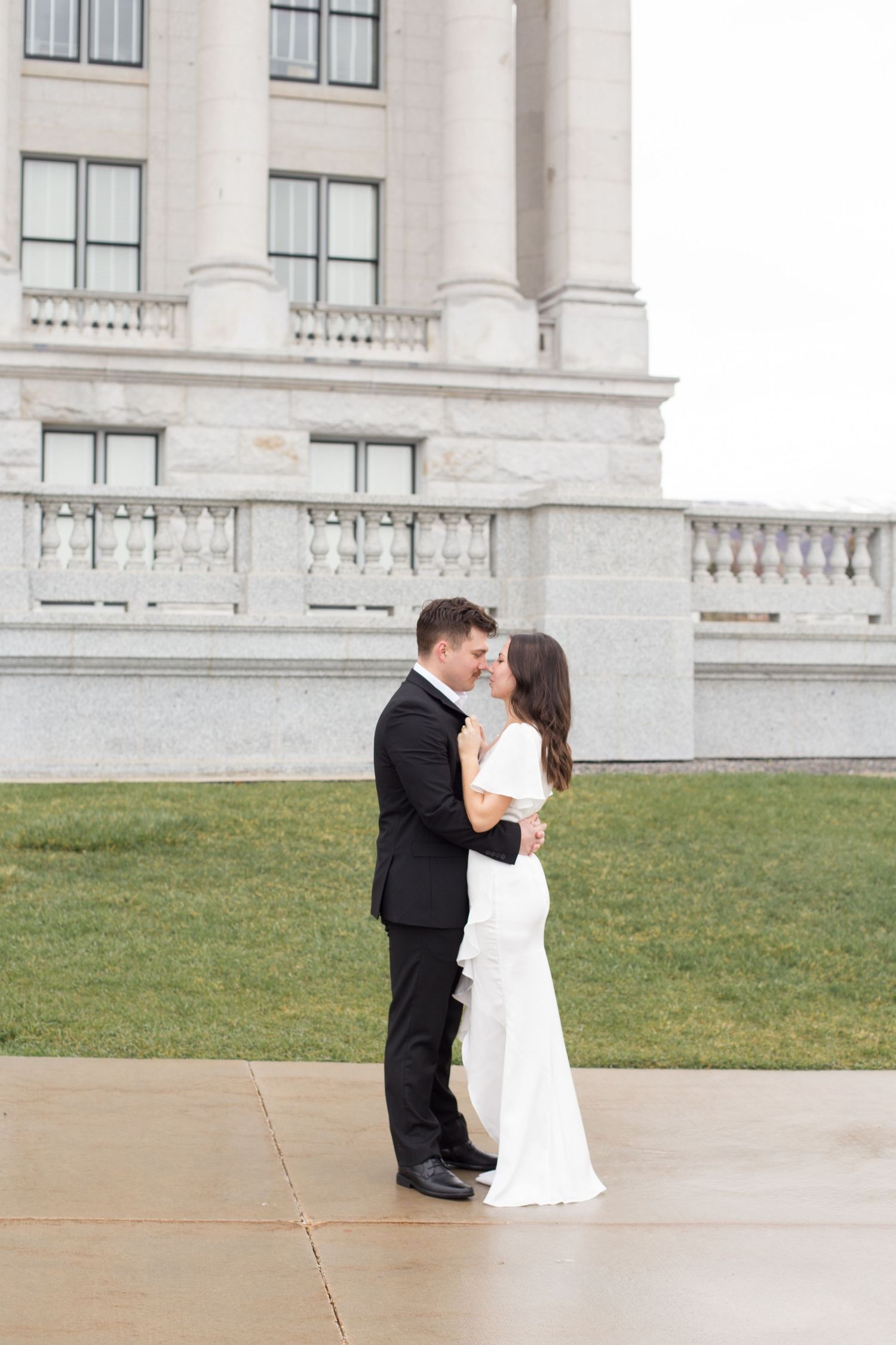 A couple shares an intimate moment outside a grand white building with columns.
