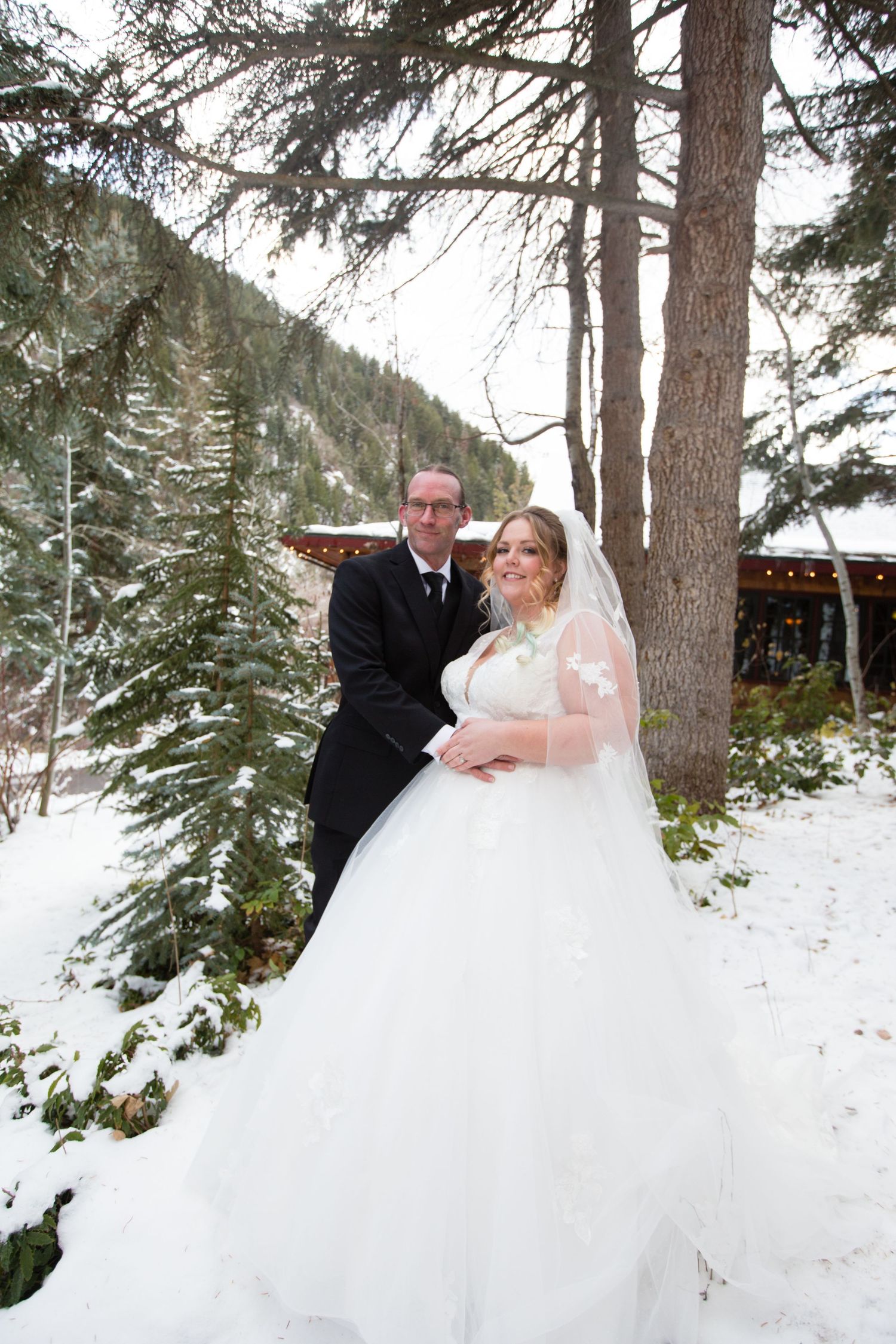 A winter wedding photoshoot in a snowy forest with tall pine trees creating a magical backdrop.