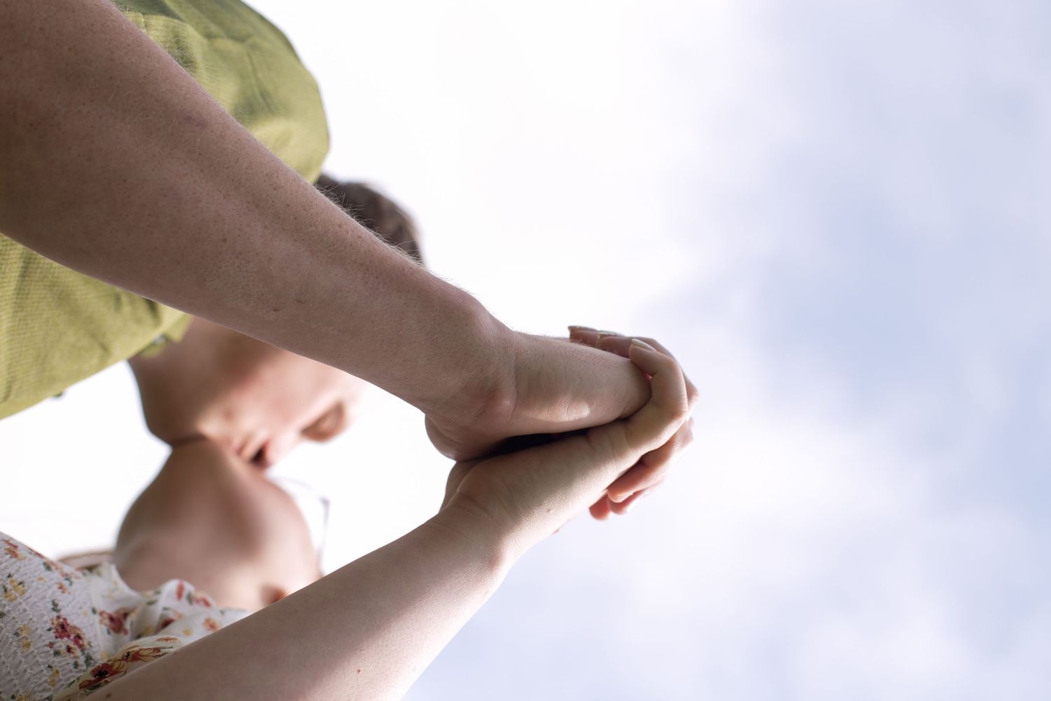 Low-angle view of two people holding hands against a bright sky, symbolizing connection and togetherness.