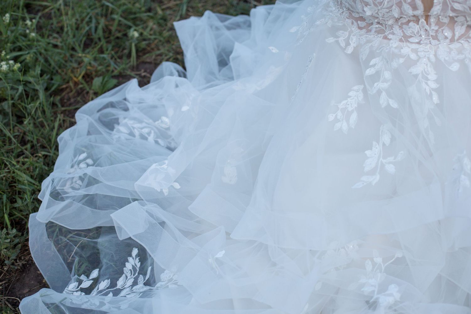 Close-up detail of delicate white lace and tulle fabric from a wedding dress against grass.