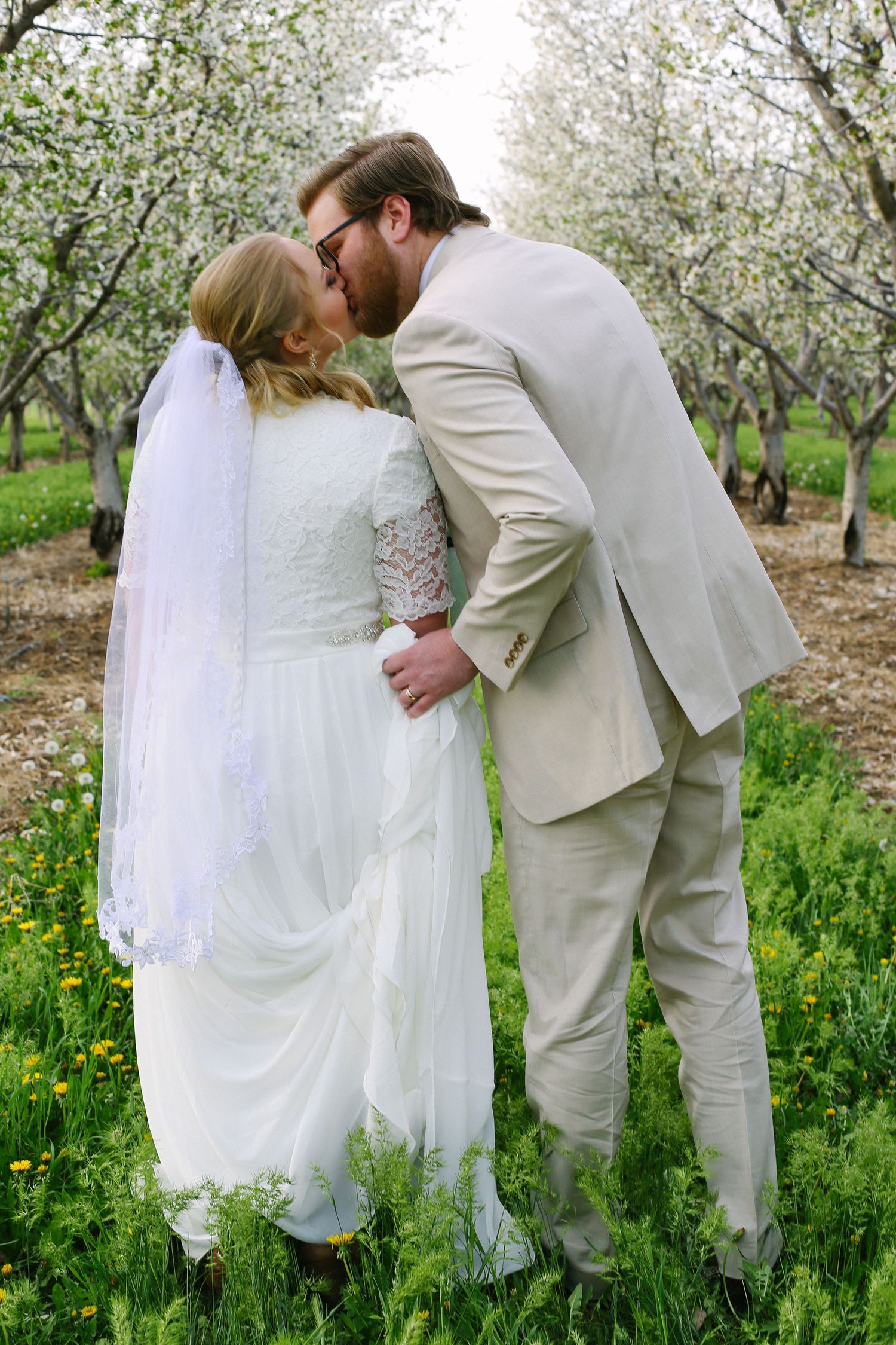 Newlyweds share intimate moment in blooming spring orchard with white flowers.