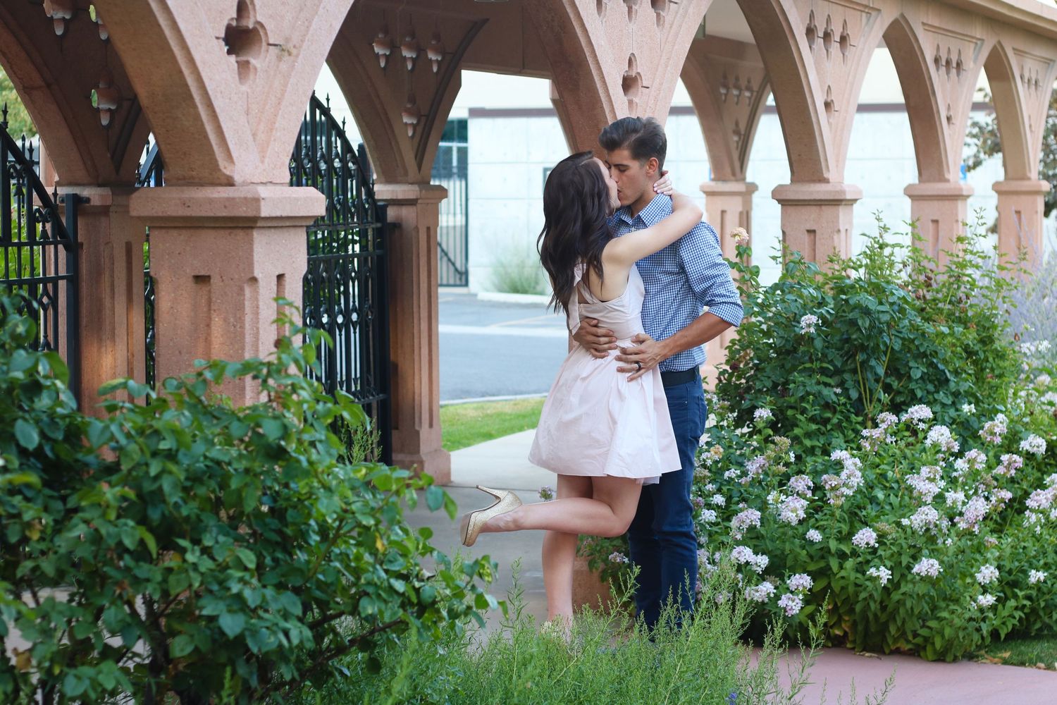 Romantic moment under ornate stone archways surrounded by blooming white flowers.