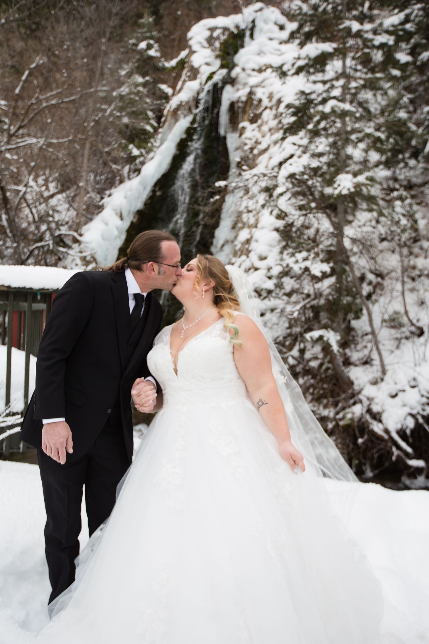 Romantic winter wedding poses captured against snowy cliff backdrop.